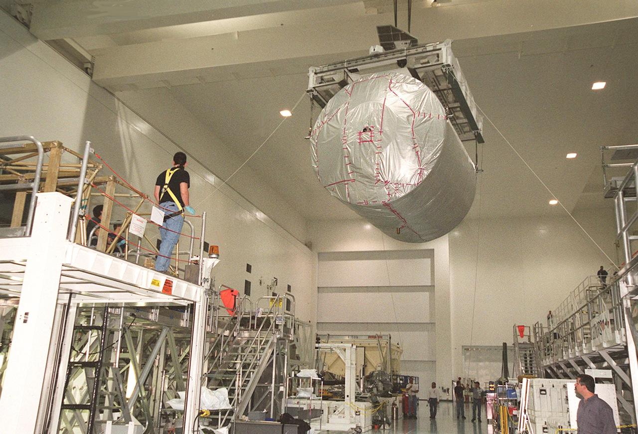 In the Space Station Processing Facility, workers wait for the Multi-Purpose Logistics Module Donatello, suspended by an overhead crane, to move onto a workstand. In the SSPF, Donatello will undergo processing by the payload test team, including integrated electrical tests with other Station elements in the SSPF, leak tests, electrical and software compatibility tests with the Space Shuttle (using the Cargo Integrated Test equipment) and an Interface Verification Test once the module is installed in the Space Shuttle’s payload bay at the launch pad. The most significant mechanical task to be performed on Donatello in the SSPF is the installation and outfitting of the racks for carrying the various experiments and cargo. Donatello will be launched on mission STS-130, currently planned for September 2004