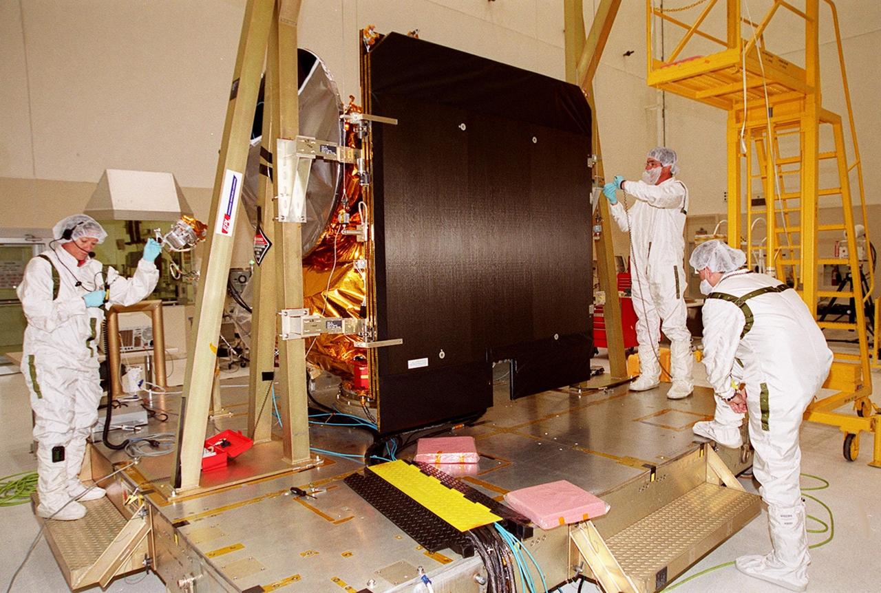 Workers in the Spacecraft Assembly and Encapsulation Facility (SAEF 2) reattach the solar panel on the 2001 Mars Odyssey Orbiter in order to conduct illumination testing. Scheduled for launch April 7, 2001, the orbiter contains three science instruments: THEMIS, the Gamma Ray Spectrometer (GRS), and the Mars Radiation Environment Experiment (MARIE). THEMIS will map the mineralogy and morphology of the Martian surface using a high-resolution camera and a thermal infrared imaging spectrometer. The GRS will achieve global mapping of the elemental composition of the surface and determine the abundance of hydrogen in the shallow subsurface. The MARIE will characterize aspects of the near-space radiation environment with regards to the radiation-related risk to human explorers