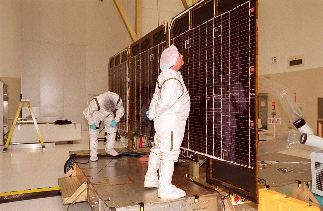 Workers examine parts of the opened solar array panels on the 2001 Mars Odyssey Orbiter. The array will undergo illumination testing. Scheduled for launch April 7, 2001, the orbiter contains three science instruments: THEMIS, the Gamma Ray Spectrometer (GRS), and the Mars Radiation Environment Experiment (MARIE). THEMIS will map the mineralogy and morphology of the Martian surface using a high-resolution camera and a thermal infrared imaging spectrometer. The GRS will achieve global mapping of the elemental composition of the surface and determine the abundance of hydrogen in the shallow subsurface. The MARIE will characterize aspects of the near-space radiation environment with regards to the radiation-related risk to human explorers
