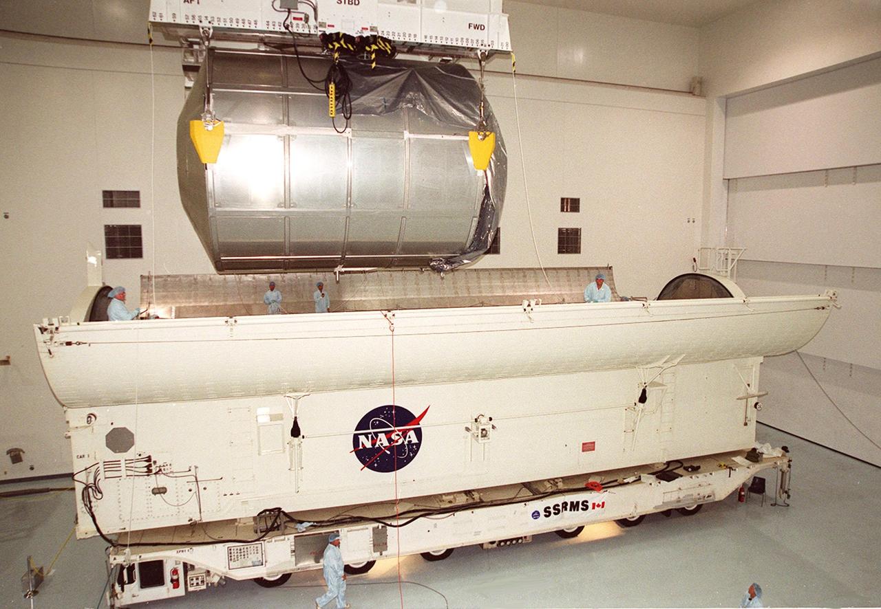 Workers inside the payload canister wait for the Multi-Purpose Logistics Module Raffaello to be lowered inside. It joins the Canadian robotic arm, SSRMS, already in place. Both elements are part of the payload on mission STS-100 to the International Space Station. Raffaello carries six system racks and two storage racks for the U.S. Lab. The arm has seven motorized joints and is capable of handling large payloads and assisting with docking the Space Shuttle. The SSRMS is self-relocatable with a Latching End Effector so it can be attached to complementary ports spread throughout the Station’s exterior surfaces. Launch of STS-100 is scheduled for April 19, 2001 at 2:41 p.m. EDT from Launch Pad 39A