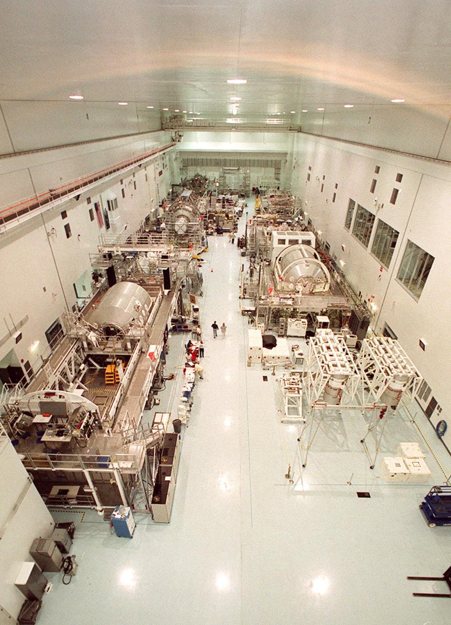 Viewed from above in the Space Station Processing Facility are equipment and several future payloads on Shuttle missions to the International Space Station. At left near the front is the Integrated Electronics Assembly. Near the opposite end, under the large windows is the Multi-Purpose Logistics Module Donatello. On the right, center, is the P3 truss. Behind it are the airlock and another MPLM, Raffaello. The large windows on the left wall give visitors on bus tours a look at operations during the day