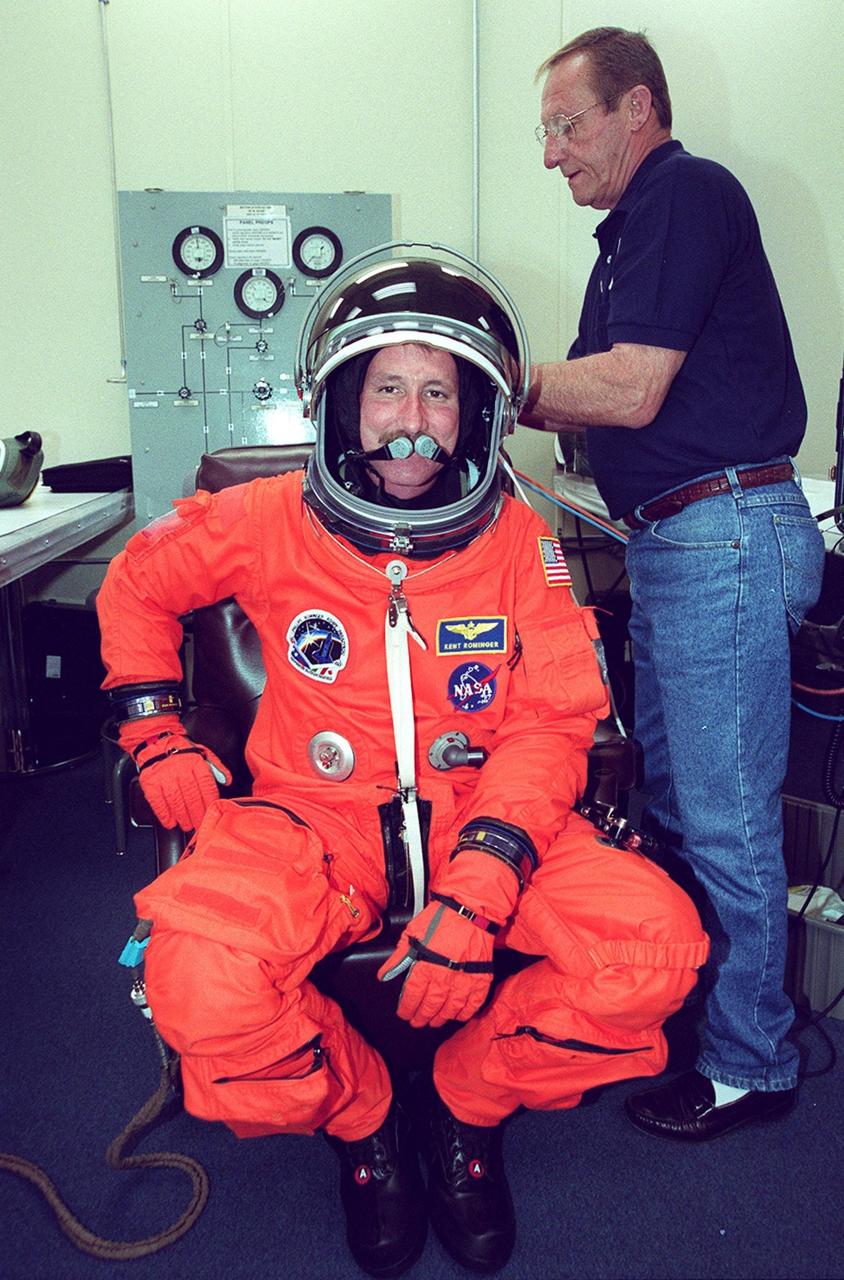 A suit technician helps STS-100 Commander Kent V. Rominger adjust his helmet during suitup for launch in the Operations and Checkout Building. The 11-day mission to the International Space Station will deliver and integrate the Spacelab Logistics Pallet/Launch Deployment Assembly, which includes the Space Station Remote Manipulator system and the UHF Antenna, and the Multi-Purpose Logistics Module Raffaello. The mission includes two planned spacewalks for installation of the SSRMS. The mission is also the inaugural flight of Raffaello, carrying resupply stowage racks and resupply/return stowage platforms. Liftoff on mission STS-100 is scheduled at 2:41 p.m. EDT April 19