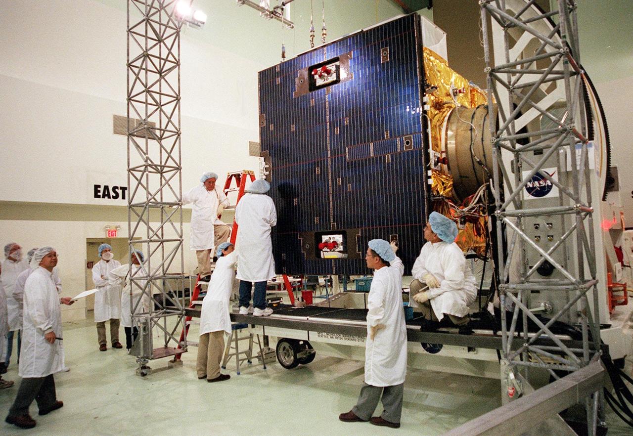 Workers at Astrotech, Titusville, Fla., check the solar panel on the GOES-M satellite. The GOES-M provides weather imagery and quantitative sounding data used to support weather forecasting, severe storm tracking and meteorological research. The satellite is scheduled to launch July 12 on an Atlas-IIA booster, Centaur upper stage from Cape Canaveral Air Force Station