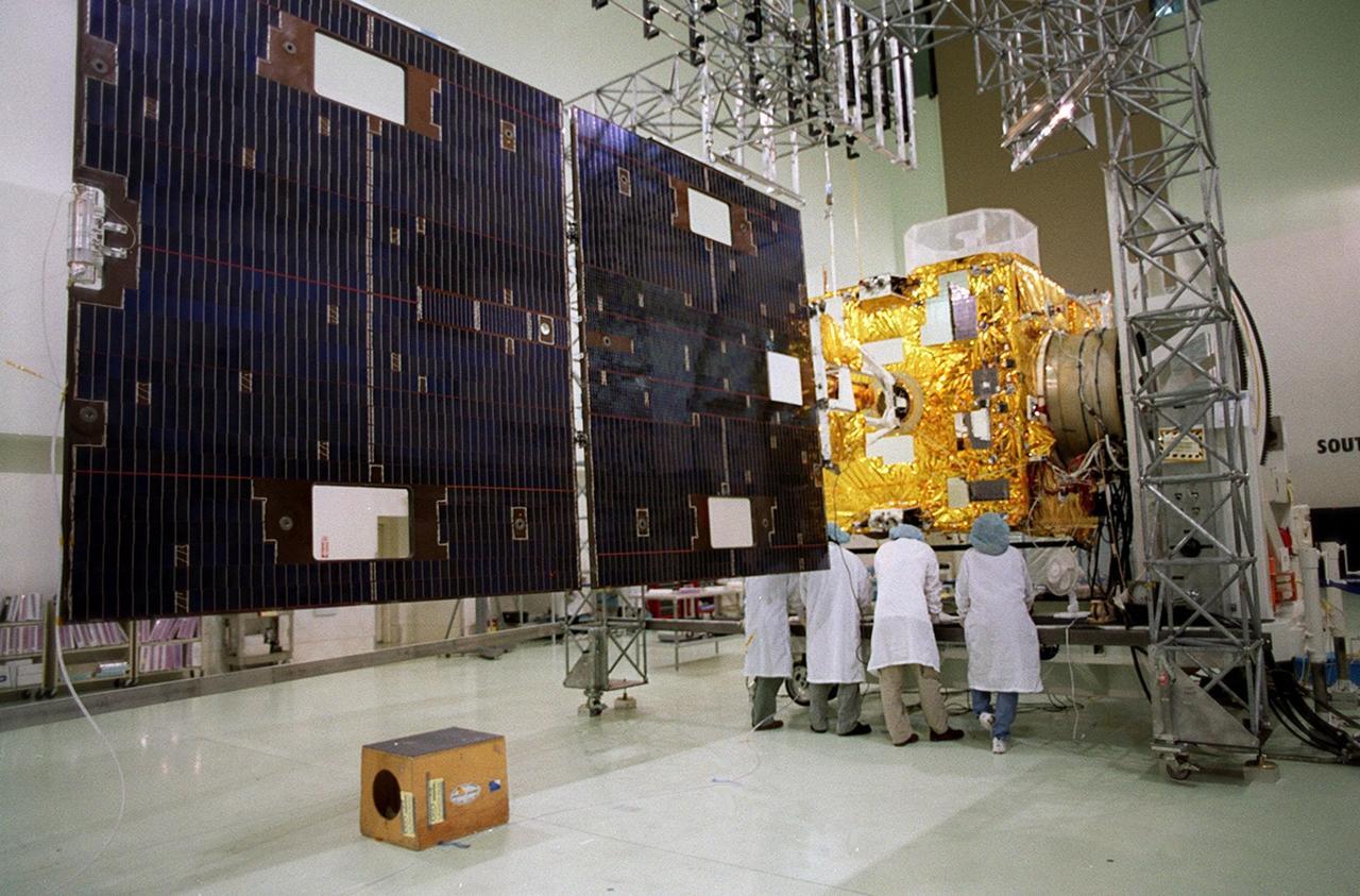 Workers at Astrotech, Titusville, Fla., look at components on the GOES-M satellite after opening the solar panel. The GOES-M provides weather imagery and quantitative sounding data used to support weather forecasting, severe storm tracking and meteorological research. The satellite is scheduled to launch July 12 on an Atlas-IIA booster, Centaur upper stage from Cape Canaveral Air Force Station