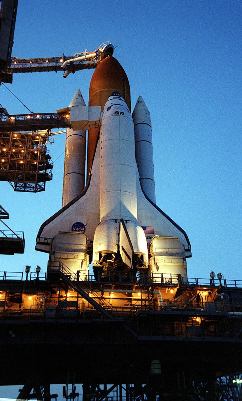 KENNEDY SPACE CENTER, Fla. -- After the rollback of the Rotating Service Structure, Space Shuttle Endeavour catches the glow of a setting sun and the lights surrounding it on Launch Pad 39A. At the top of the external tank can be seen the “beanie cap,” a venting apparatus at the end of the Gaseous Oxygen Vent Arm. Below it stretches the Orbiter Access Arm with the White Room extended to the orbiter. The White Room provides a controlled environment for entry into the orbiter. Endeavour is expected to lift off on mission STS-100 on April 19, carrying the Multi-Purpose Logistics Module Raffaello and the Canadian robotic arm, SSRMS, with a crew of seven to the International Space Station