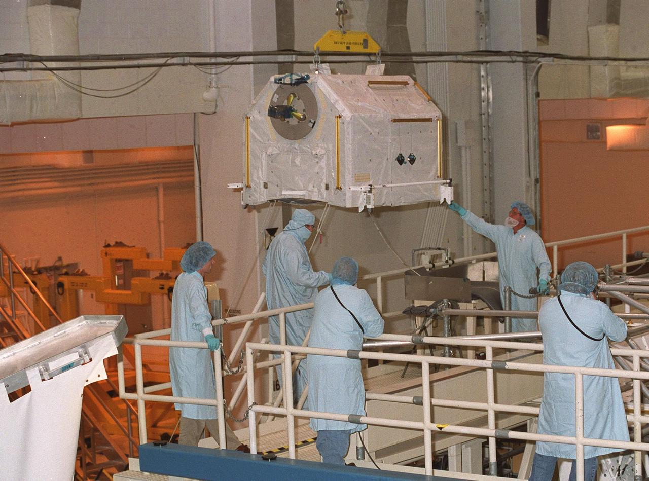 KENNEDY SPACE CENTER, FLA. -- Workers in the Operations and Checkout Building stand by while one of four gas tanks is moved toward the Spacelab Logistics Double Pallet. Part of the STS-104 payload, the storage tanks two gaseous oxygen and two gaseous nitrogen comprise the high pressure gas assembly that will be attached to the Joint Airlock Module during two spacewalks. The tanks will support future spacewalk operations from the Station and augment the Service Module gas resupply system