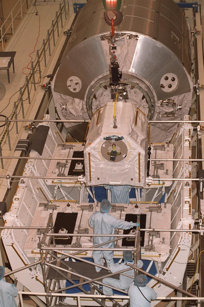 KENNEDY SPACE CENTER, FLA. -- An overhead crane in the Operations and Checkout Building lowers one of four gas tanks onto the Spacelab Logistics Double Pallet while workers help guide it. Part of the STS-104 payload, the storage tanks two gaseous oxygen and two gaseous nitrogen comprise the high pressure gas assembly that will be attached to the Joint Airlock Module during two spacewalks. The tanks will support future spacewalk operations from the Station and augment the Service Module gas resupply system