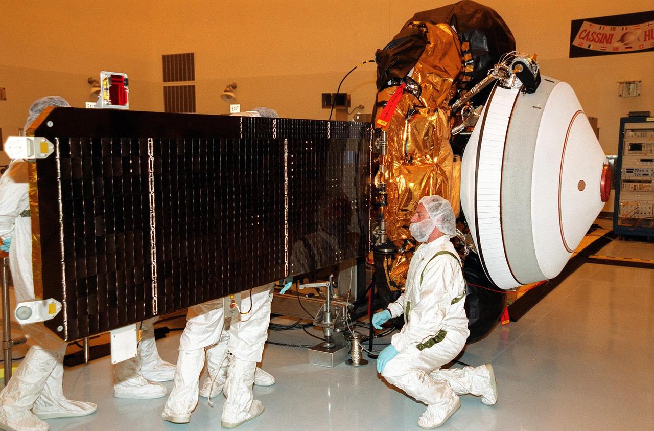 KENNEDY SPACE CENTER, Fla. -- Workers in the Payload Hazardous Servicing Facility check closely the solar arrays on the Genesis spacecraft. Genesis is designed to collect samples of solar wind particles and return them to Earth so that scientists can study the exact composition of the Sun and probe the solar system’s origin. The white object on the end in front of the arrays is the Sample Return Canister backshell, inside of which are the collector arrays. Genesis is scheduled to be launched on a Delta II Lite launch vehicle from Complex 17-A, Cape Canaveral Air Force Station, July 30, at 12:36 p.m. EDT