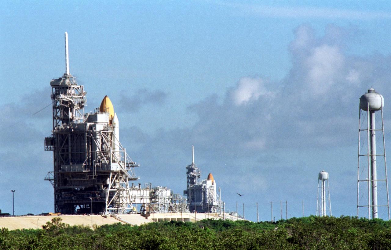 KENNEDY SPACE CENTER, Fla. -- Space Shuttle Discovery (foreground) and Space Shuttle Atlantis (background) both stand ready on their Launch Pads ( 39A and 39B respectively). Space Shuttle Discovery rolled out July 2 to be prepared for launch on mission STS-105 in August. Space Shuttle Atlantis is scheduled to launch Thursday, July 12, on mission STS-104. Towering above each Shuttle on the left is the 80-foot lightning rod that helps protect each Shuttle from lightning strikes. At right are the 290-foot water tanks that provide 300,000 gallons of water during liftoff. They are part of the sound suppression water system at each pad