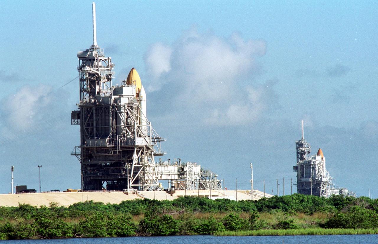 KENNEDY SPACE CENTER, Fla. -- Space Shuttle Discovery (foreground) and Space Shuttle Atlantis (background) both stand ready on their Launch Pads ( 39A and 39B respectively). Space Shuttle Discovery rolled out July 2 to be prepared for launch on mission STS-105 in August. Space Shuttle Atlantis is scheduled to launch Thursday, July 12, on mission STS-104. Towering above each Shuttle on the left is the 80-foot lightning rod that helps protect each Shuttle from lightning strikes