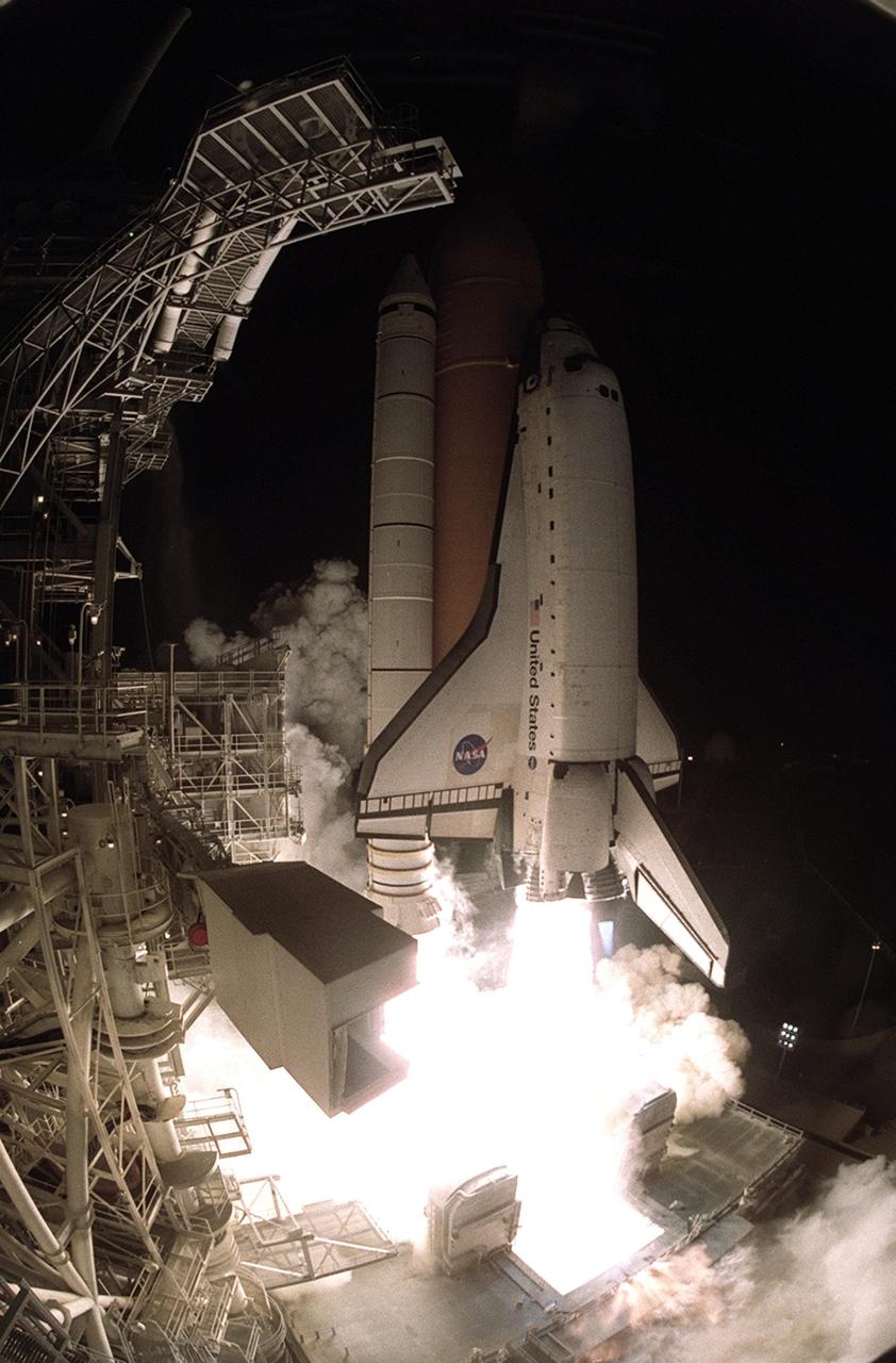 KENNEDY SPACE CENTER, Fla. -- Space Shuttle Atlantis spews flame and billows of steam as it lifts off the pad on mission STS-104. At left is the Fixed Service Structure, with the White Room (foreground) safely moved away. Situated at the end of the orbiter access arm, the White Room provides entry into the cockpit of the Shuttle. Atlantis lifted off from Launch Pad 39B on time at 5:03:59 a.m. EDT. With a crew of five, it is heading on the 10th assembly flight to the International Space Station. The primary payload on the mission is the joint airlock module, which will require two spacewalks to attach it to the Space Station. The airlock will be the primary path for Space Station spacewalk entry and departure for U.S. spacesuits, and will also support the Russian Orlan spacesuit for EVA activity