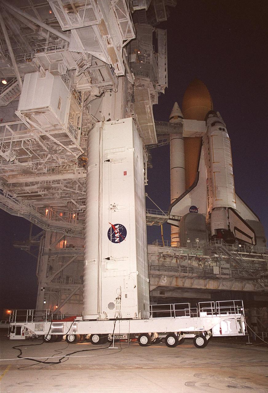 KENNEDY SPACE CENTER, Fla. -- Just before sunrise the payload canister arrives at Launch Pad 39A. In the background is Space Shuttle Discovery, waiting to launch on mission STS-105. Inside the canister are the primary payloads on the mission, the Multi-Purpose Logistics Module Leonardo and the Integrated Cargo Carrier. The ICC holds several smaller payloads, the Early Ammonia Servicer and two experiment containers. The Early Ammonia Servicer consists of two nitrogen tanks that provide compressed gaseous nitrogen to pressurize the ammonia tank and replenish it in the thermal control subsystems of the Space Station. The ICC and MPLM will be lifted into the payload changeout room on the Rotation Service Structure where they will be moved into the Discovery’s payload bay. The STS-105 mission includes a crew changeover on the International Space Station. Expedition Three will be traveling on Discovery to replace Expedition Two, who will return to Earth on board Discovery. Launch of STS-105 is scheduled for Aug. 9