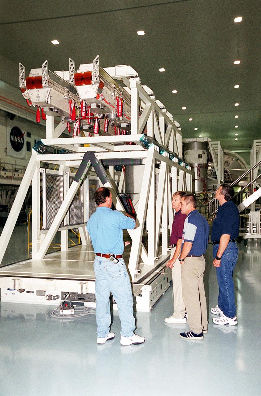 KENNEDY SPACE CENTER, Fla. -- In the Space Station Processing Facility, the Expedition Three crew (right) listen to a worker discuss solar panels seen here on a workstand. The crew members are (left to right) Commander Frank Culbertson and cosmonauts Mikhail Tyurin and Vladimir Dezhurov. The STS-105 payload includes the Early Ammonia Servicer (EAS), Multi-Purpose Logistics Module Leonardo and various experiments attached on the port and starboard adapter beams. The EAS contains spare ammonia for the Station’s cooling system. Ammonia is the fluid used in the radiators that cool the Station’s electronics. The EAS will be installed on the P6 truss holding the giant U.S. solar arrays, batteries and cooling radiators. Leonardo is filled with laboratory racks of science equipment and racks and platforms of experiments and supplies. Discovery is scheduled to be launched Aug. 9, 2001