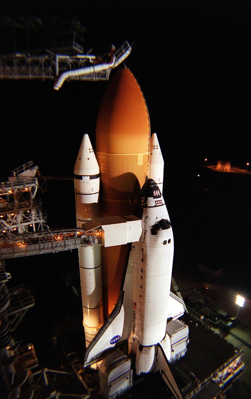 KENNEDY SPACE CENTER, Fla. -- Lights surrounding Launch Pad 39A create shadows from Space Shuttle Discovery after rollback of the Rotating Service Structure. Seen extending to the orbiter is the orbiter access arm, ending at the White Room, an environmental chamber that mates with the orbiter and allows personnel to enter the crew compartment. Above the external tank, the “beanie cap” is poised, waiting for loading of the propellants. The cap, or vent hood, is on the end of the gaseous oxygen vent arm that allows gaseous oxygen vapors to vent away from the Space Shuttle. On mission STS-105, Discovery will be transporting the Expedition Three crew and several scientific experiments and payloads to the International Space Station, including the Early Ammonia Servicer (EAS) tank. The EAS, which will support the thermal control subsystems until a permanent system is activated, will be attached to the Station during two spacewalks. The three-member Expedition Two crew will be returning to Earth aboard Discovery after a five-month stay on the Station. Launch is scheduled for 5:38 p.m. EDT Aug. 9