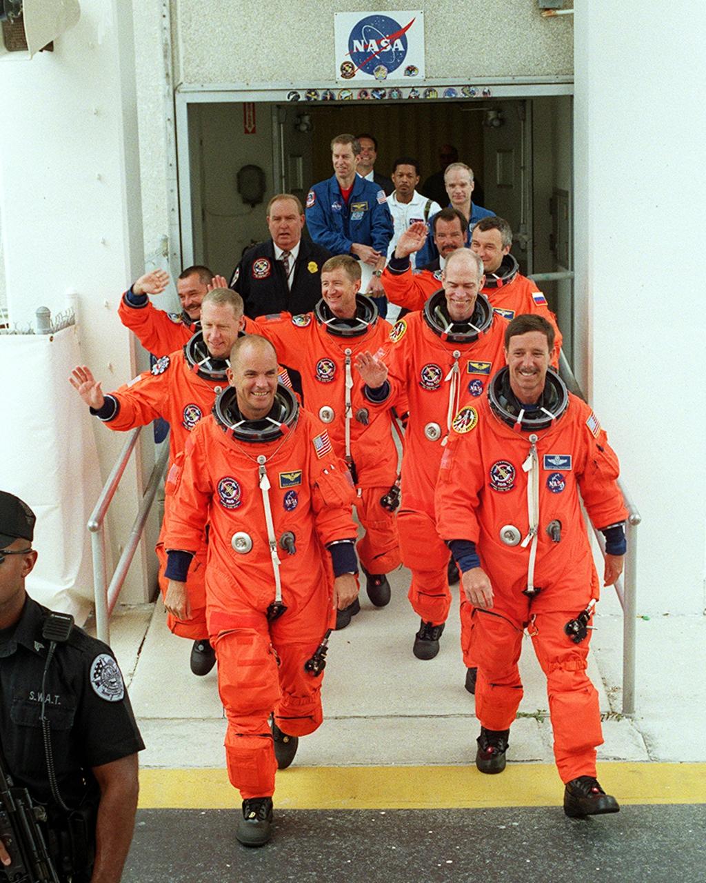 KENNEDY SPACE CENTER, Fla. -- The STS-105 and Expedition Three (E3) crews grin as they exit the Operations and Checkout Building on their way to Launch Pad 39A for a second launch attempt. Leading the way are (left to right) Pilot Rick Sturckow and Commander Scott Horowitz; in the second row, Mission Specialists Patrick Forrester and Daniel Barry; in the third row, E3 cosmonaut Mikhail Tyurin, Commander Frank Culbertson, and cosmonaut Vladimir Dezhurov. Forrester and Tyurin are both making their first space flights. Launch countdown activities for the 12-day mission were called off at about 5:12 p.m. Aug. 9 during the T-9 minute hold due to the high potential for lightning, a thick cloud cover and the potential for showers. Launch is currently scheduled for 5:15 p.m. EDT Aug. 10. Highlighting the mission will be the rotation of the International Space Station crew, the third flight of an Italian-built Multi-Purpose Logistics Module delivering additional scientific racks, equipment and supplies for the Space Station, and two spacewalks. Included in the payload is the Early Ammonia Servicer (EAS) tank, which will be attached to the Station during the spacewalks. The EAS will be installed on the P6 truss, which holds the Station’s giant U.S. solar arrays, batteries and the cooling radiators. The EAS contains spare ammonia for the Station’s cooling system. The three-member Expedition Two crew will be returning to Earth aboard Discovery after a five-month stay on the Station