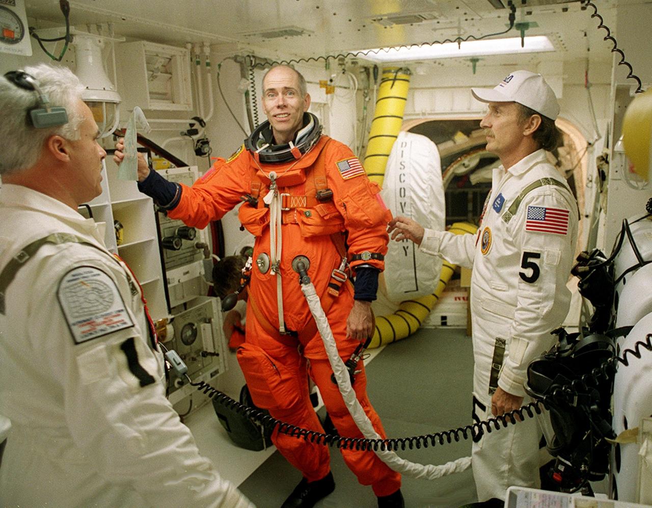 KENNEDY SPACE CENTER, Fla. -- STS-105 Commander Scott Horowitz sends a message home while preparing to enter Space Shuttle Discovery for launch.  Assisting with flight equipment are (left) Orbiter Vehicle Closeout Chief Chris Meinert, (right) USA Mechanical Technician Al Schmidt and (behind) NASA Quality Assurance Specialist Ken Strite. The payload on the STS-105 mission to the International Space Station includes the third flight of the Italian-built Multi-Purpose Logistics Module Leonardo, delivering additional scientific racks, equipment and supplies for the Space Station, and the Early Ammonia Servicer (EAS) tank.  The EAS, which will be attached to the Station during two spacewalks, contains spare ammonia for the Station's cooling system.  Also, the Expedition Three crew is aboard to replace the Expedition Two crew on the Space Station, who will be returning to Earth aboard Discovery after a five-month stay on the Station