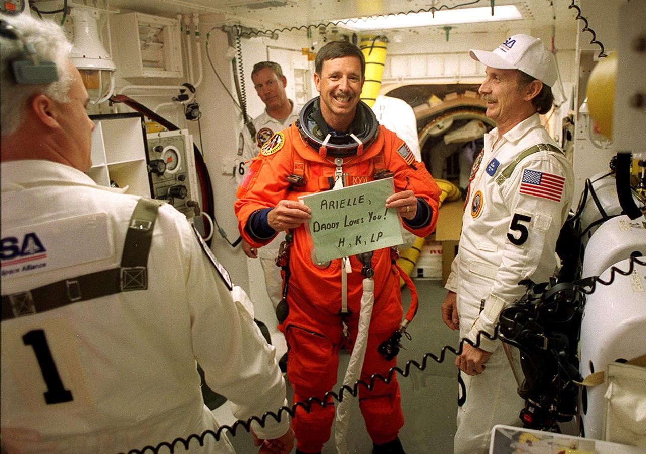 KENNEDY SPACE CENTER, Fla. - STS-105 Commander Scott Horowitz sends a message home while preparing to enter Space Shuttle Discovery for launch. Assisting with flight equipment are (left) Orbiter Vehicle Closeout Chief Chris Meinert, (right) USA Mechanical Technician Al Schmidt and (behind) NASA Quality Assurance Specialist Ken Strite. The payload on the STS-105 mission to the International Space Station includes the third flight of the Italian-built Multi-Purpose Logistics Module Leonardo, delivering additional scientific racks, equipment and supplies for the Space Station, and the Early Ammonia Servicer (EAS) tank. The EAS, which will be attached to the Station during two spacewalks, contains spare ammonia for the Station’s cooling system. Also, the Expedition Three crew is aboard to replace the Expedition Two crew on the International Space Station, who will be returning to Earth aboard Discovery after a five-month stay on the Station