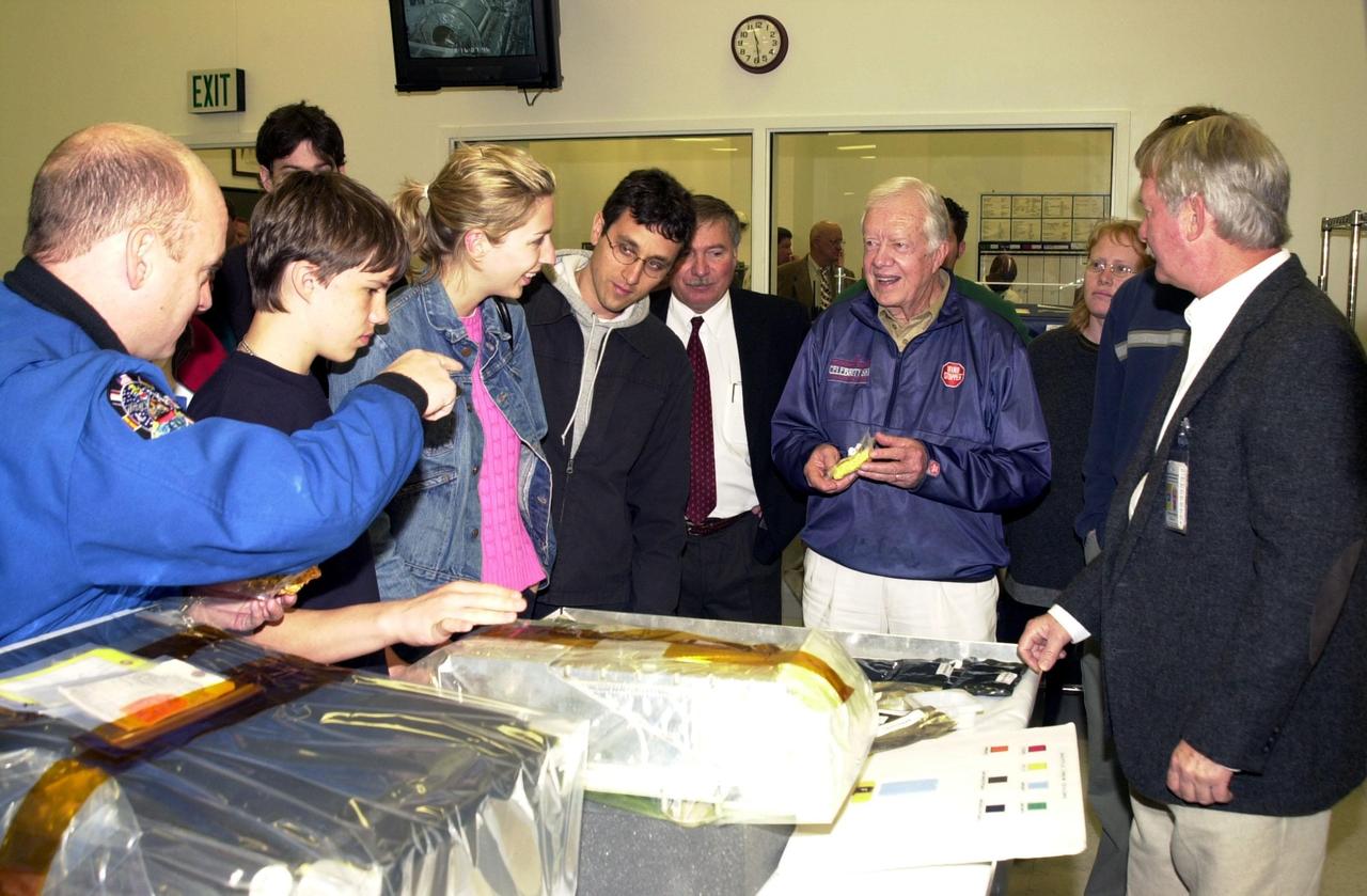 KENNEDY SPACE CENTER, FLA. -- During a tour of KSC, former President Jimmy Carter is shown packages of food that are used on the International Space Station.  Astronaut Scott Kelly (far left) relates how the food is prepared and how it tastes.  Behind and to the left of Carter is Tip Talone, director of Payload Processing, International Space Station.  At the far right is Ron Woods, a technician in the Flight Crew Equipment Facility