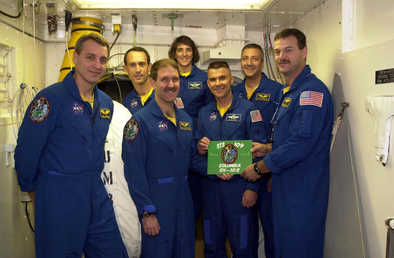 KENNEDY SPACE CENTER, FLA. -- At Launch Pad 39A, the STS-109 crew stands in the White Room, outside the entry into Space Shuttle Columbia, displaying the mission patch and placard.  Standing, left to right, are Mission Specialists Richard Linnehan, James Newman, John Grunsfeld and Nancy Currie; Pilot Duane Carey; Mission Specialist Michael Massimino; and Commander Scott Altman.  The White Room is an environmentally controlled structure at the end of the Orbiter Access Room that provides access to the orbiter. The crew is taking part in Terminal Countdown Demonstration Test activities that include emergency egress training and a simulated countdown at the pad.  Columbia is scheduled to be launched Feb. 28 on mission STS-109, a Hubble Servicing Mission. The goal of the mission is to replace Solar Array 2 with Solar Array 3, replace the Power Control Unit, remove the Faint Object Camera and install the ACS, install the Near Infrared Camera and Multi-Object Spectrometer (NICMOS) Cooling System, and install New Outer Blanket Layer insulation. .  The launch will be the first for Columbia after returning from California where it underwent extensive maintenance, inspections and enhancements. More than 100 upgrades make Columbia safer and more reliable than ever before