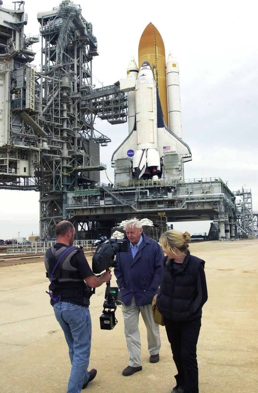 KENNEDY SPACE CENTER, FLA. - Sir David Attenborough (center) works with a film crew on Launch Pad 39A. Space Shuttle Columbia, atop the Mobile Launcher Platform, is seen in the background. At left are the Rotating Service Structure, which is open, and the Fixed Service Structure. Attenborough is filming commentary for a documentary