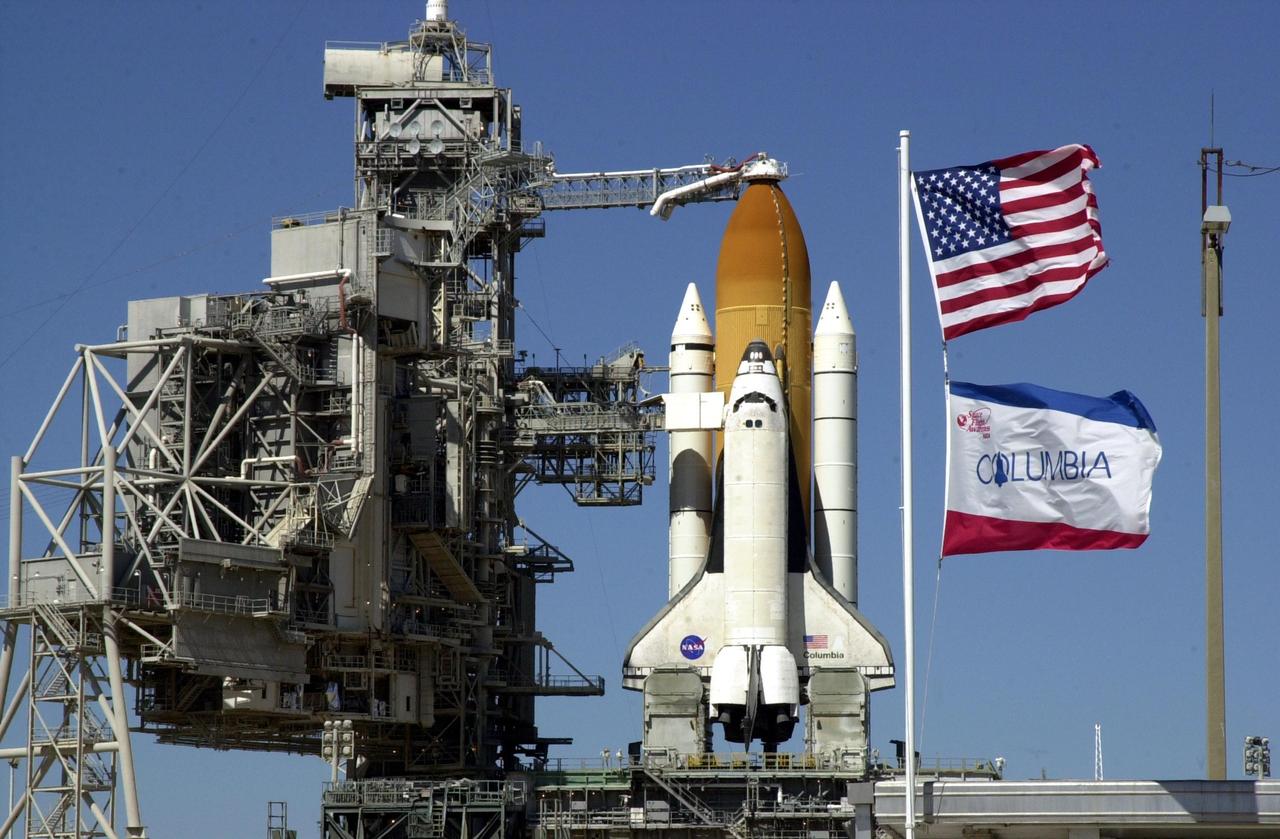 KENNEDY SPACE CENTER, FLA. -- The Rotating Service Structure is rolled back from Space Shuttle Columbia in preparation for launch Feb. 28, 2002, at 6:48 a.m. EST (11:48 GMT) on mission STS-109. Flags of the U.S. and the orbiter (foreground) illustrate the brisk winds blowing at Launch Complex 39A. In the photo is seen the Orbiter Access Arm stretched to Columbia's cockpit. A Hubble Servicing Mission, the goal of STS-109 is to replace Solar Array 2 with Solar Array 3, replace the Power Control Unit, remove the Faint Object Camera and install the ACS, install the Near Infrared Camera and Multi-Object Spectrometer (NICMOS) Cooling System, and install New Outer Blanket Layer insulation.