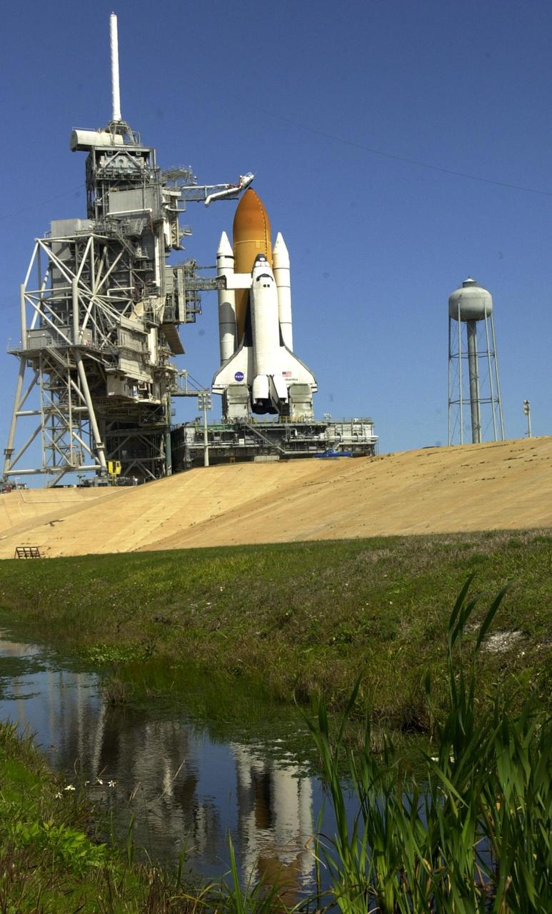 KENNEDY SPACE CENTER, Fla. - Rollback of the Rotating Service Structure for the second time, after a scrub of mission STS-109 the day before, provides an unfettered look at Space Shuttle Columbia on Launch Pad 39A. The nearby water gives an impressionistic view. Above the orange-colored external tank is poised the "beanie cap," the gaseous oxygen vent hood. Extending to the side of Columbia is the Orbiter Access Arm with the environmentally controlled White Room at the end. The White Room provides entry for the crew into the orbiter. Columbia sits atop the Mobile Launcher Platform. At right is the 290-foot-tall water tower that holds 300,000 gallons of water, part of the sound suppression system during a launch. Columbia is rescheduled for launch on mission STS-109 March 1 at 6:22 a.m. EST (11:22 GMT). The 11-day mission will provide maintenance and upgrade to the Hubble Space Telescope, replacing Solar Array 2 with Solar Array 3, replacing the Power Control Unit, installing the ACS (after removing the Faint Object Camera ), the Near Infrared Camera, the Multi-Object Spectrometer (NICMOS) Cooling System, and the New Outer Blanket Layer insulation.