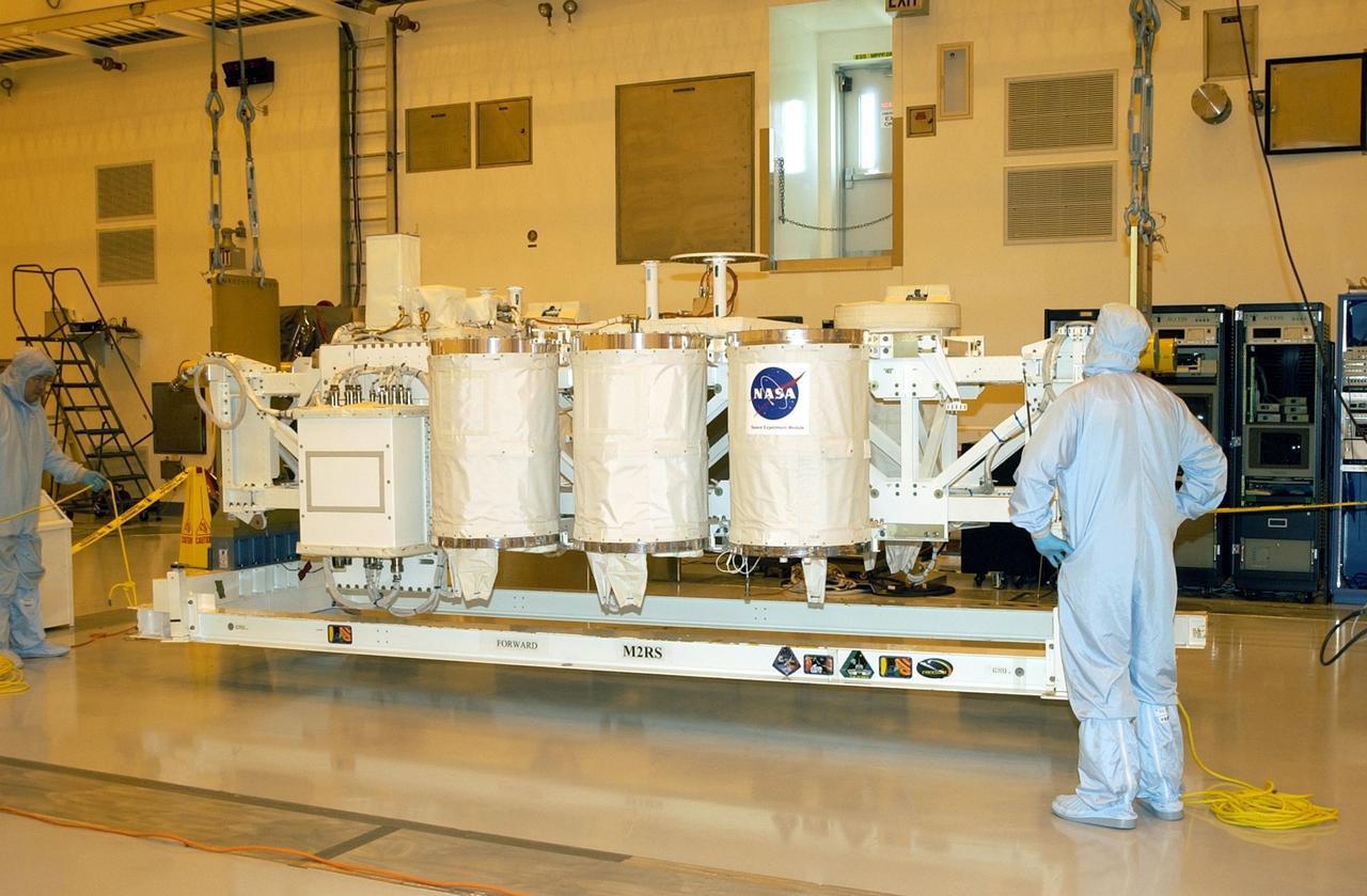 KENNEDY SPACE CENTER, FLA. -- In the Multi-Payload Processing Facility (MPPF), workers watch as the Hitchhiker Bridge, with several Get-Away Special canisters (GAS cans) for mission ST-107, is lifted off the ground. The bridge is being moved to a workstand in the MPPF. The bridge is a carrier for the Fast Reaction Experiments Enabling Science, Technology, Applications and Research (FREESTAR) that incorporates eight high priority secondary attached shuttle experiments on mission STS-107. A research mission, the primary payload is the first flight of the SHI Research Double Module (SHI/RDM), also known as SPACEHAB. The experiments range from material sciences to life sciences. STS-107 is scheduled to launch July 11, 2002