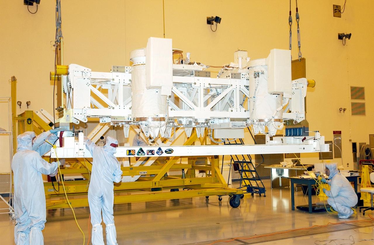 KENNEDY SPACE CENTER, FLA. -- In the Multi-Payload Processing Facility (MPPF), workers check the Hitchhiker Bridge that is being lifted by a crane for transfer to a workstand. The bridge is a carrier for the Fast Reaction Experiments Enabling Science, Technology, Applications and Research (FREESTAR) that incorporates eight high priority secondary attached shuttle experiments on mission STS-107. A research mission, the primary payload is the first flight of the SHI Research Double Module (SHI/RDM), also known as SPACEHAB. The experiments range from material sciences to life sciences. STS-107 is scheduled to launch July 11, 2002