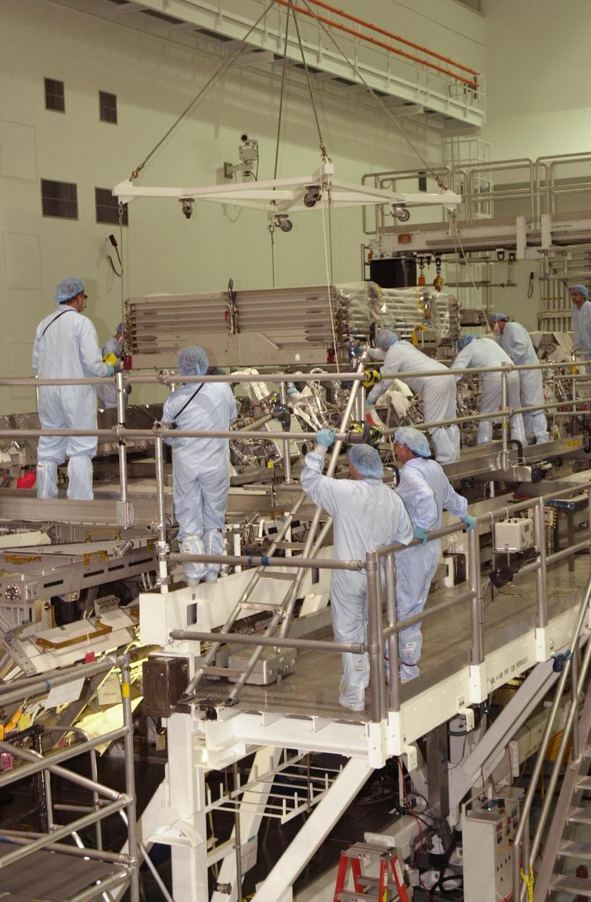 KENNEDY SPACE CENTER, FLA. -- In the Space Station Processing Facility, workers oversee the lowering of the newly arrived radiator assembly onto a workstand. The radiator is part of the payload on mission STS-113, which also includes the first port truss segment, P1 Truss, to be attached to the central truss segment, S0 Truss, on the International Space Station. Once delivered, the will remain stowed until flight 12A.1. STS-113 is scheduled to launch Oct. 6, 2002