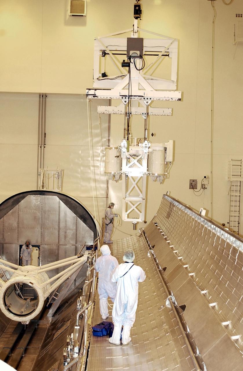 KENNEDY SPACE CENTER, FLA. - Workers in the Multi-Payload Processing Facility watch the progress of the overhead crane carrying the Hitchhiker Bridge with GetAway Special canisters (GAS cans). The bridge, a carrier for the Fast Reaction Experiments Enabling Science, Technology, Applications and Research (FREESTAR) that incorporates eight high priority secondary attached shuttle experiments, is being transferred to the payload canister below it.   The bridge will be installed in Columbia's payload bay as part of mission STS-107. A research mission, STS-107 will also carry the SHI Research Double Module (SHI/RDM), known as SPACEHAB. Experiments on the module range from material sciences to life sciences (many rats).  STS-107 is scheduled to launch July 19, 2002