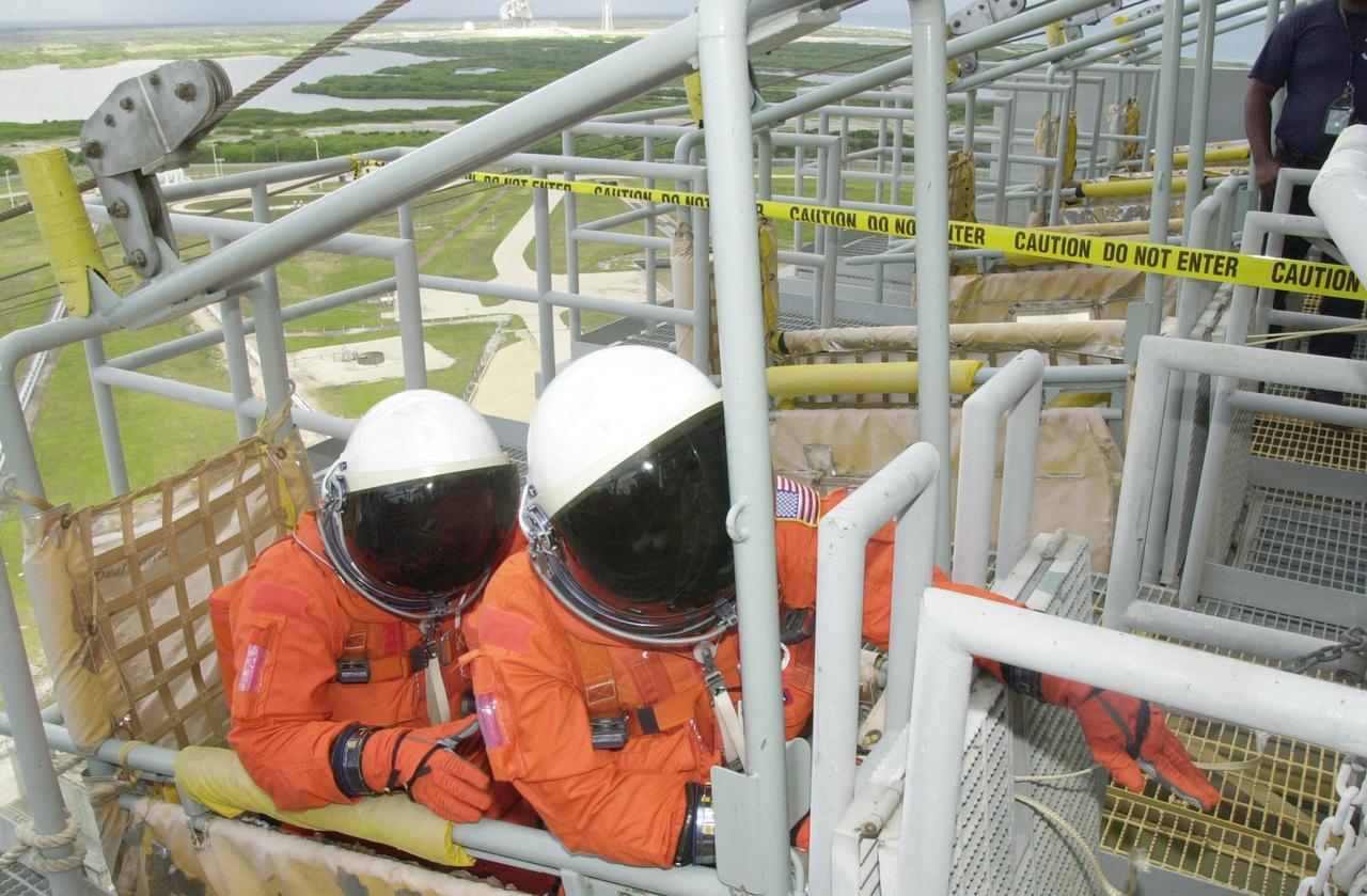 KENNEDY SPACE CENTER, FLA. - STS-111 Commander Kenneth Cockrell (left) settles in the seat of the slidewire basket while Pilot Paul Lockhart (right) gets ready to pull the release lever. They and the rest of the STS-111 crew and the Expedition 5 crew are taking part in Terminal Countdown Demonstration Test activities, which include emergency egress training and a simulated launch countdown.  Mission STS-111 is Utilization Flight 2, carrying equipment and supplies in the Multi-Purpose Logistics Module Leonardo to the International Space Station, plus the Mobile Base System (MBA) and an Orbital Replacement Unit.  The MBS will be installed on the Mobile Transporter to complete the Canadian Mobile Servicing System, or MSS, enabling Canadarm 2 to "inchworm" from the U.S. Lab Destiny to the MSS and travel along the truss to work sites.  The Expedition 5 crew is traveling on Endeavour to replace the Expedition 4 crew on the Station.  Launch of Endeavour is scheduled for May 30, 2002