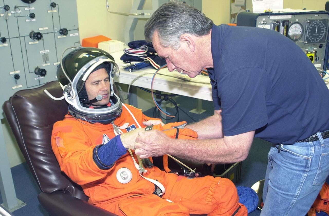 KENNEDY SPACE CENTER, FLA. --  STS-111 Pilot Paul Lockhart is helped with his glove during suit check, part of pre-launch activities.  The mission, known as Utilization Flight 2, is carrying supplies and equipment to the Station. The payload includes the Multi-Purpose Logistics Module Leonardo, the Mobile Base System, which will be installed on the Mobile Transporter to complete the Canadian Mobile Servicing System, or MSS, and a replacement wrist/roll joint for Canadarm 2. The mechanical arm will then have the capability to "inchworm" from the U.S. Lab Destiny to the MSS and travel along the truss to work sites. Also part of the mission, Expedition 5 will travel to the International Space Station as the replacement crew for Expedition 4, who will return to Earth aboard the orbiter.  Launch is scheduled for May 30, 2002