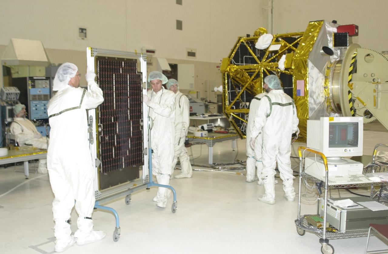 KENNEDY SPACE CENTER, FLA. -- Workers in the Spacecraft Assembly and Encapsulation Facility 2 move a solar panel toward the Comet Nucleus Tour (CONTOUR) spacecraft (in the background) for installation. The spacecraft will provide the first detailed look into the heart of a comet -- the nucleus. The spacecraft will fly as close as 60 miles (100 kilometers) to at least two comets and will take the sharpest pictures yet of the nucleus while analyzing the gas and dust that surround these rocky, icy building blocks of the solar system. Launch of CONTOUR aboard a Boeing Delta II rocket is scheduled for July 1 from Launch Pad 17-A, Cape Canaveral Air Force Station
