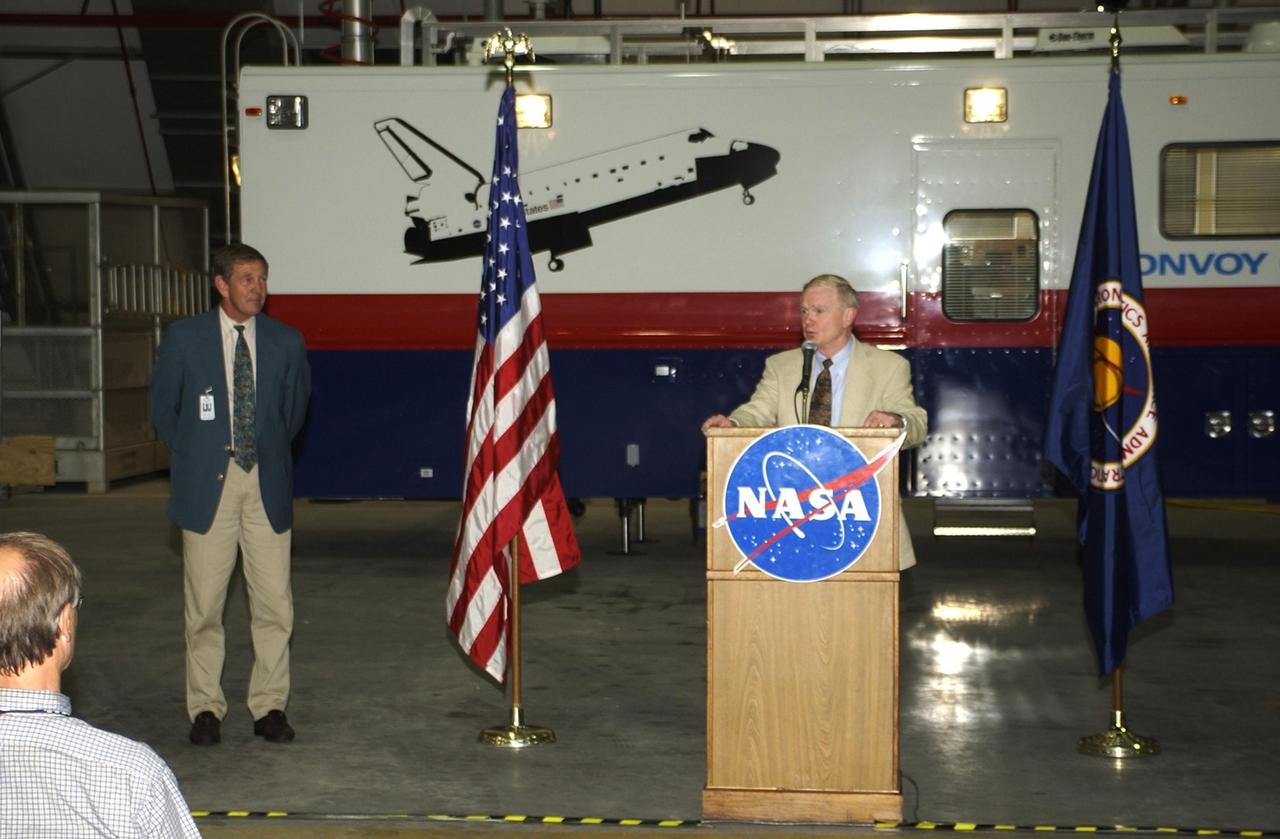 KENNEDY SPACE CENTER, FLA. --  At the podium, Center Director Roy Bridges Jr. offers remarks at the commissioning ceremony for the new Convoy Command Vehicle behind him.  At left is Mike McCulley, chief operating officer, United Space Alliance. The new 40-foot vehicle is replacing a 15-year old model, and will be used following Shuttle landings as the prime vehicle to control critical communications between the orbiter, the crew and the Launch Control Center, to monitor the health of the Shuttle Orbiter systems and to direct convoy operations at the Shuttle Landing Facility. Upgrades and high-tech features incorporated into the design and development of this vehicle make it more reliable and efficient for the convoy crew. Seating capacity was increased from 4 to 12, and video recorders and television monitors were added to provide the convoy team with the maximum amount of visual information