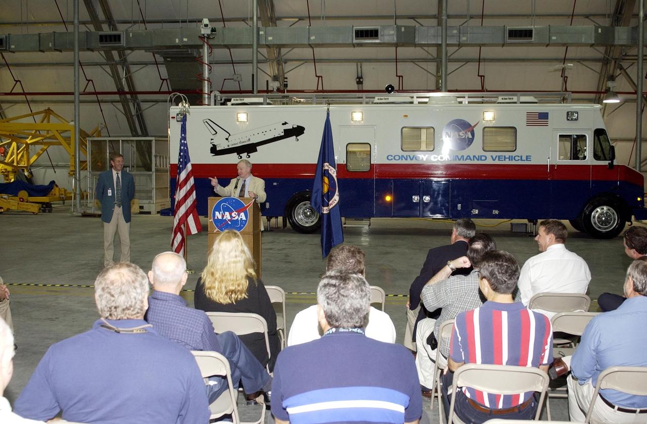 KENNEDY SPACE CENTER, FLA. -- At the podium, Center Director Roy Bridges Jr. offers remarks at the commissioning ceremony for the new Convoy Command Vehicle behind him.  At left is Mike McCulley, chief operating officer, United Space Alliance. The new 40-foot vehicle is replacing a 15-year old model, and will be used following Shuttle landings as the prime vehicle to control critical communications between the orbiter, the crew and the Launch Control Center, to monitor the health of the Shuttle Orbiter systems and to direct convoy operations at the Shuttle Landing Facility. Upgrades and high-tech features incorporated into the design and development of this vehicle make it more reliable and efficient for the convoy crew. Seating capacity was increased from 4 to 12, and video recorders and television monitors were added to provide the convoy team with the maximum amount of visual information