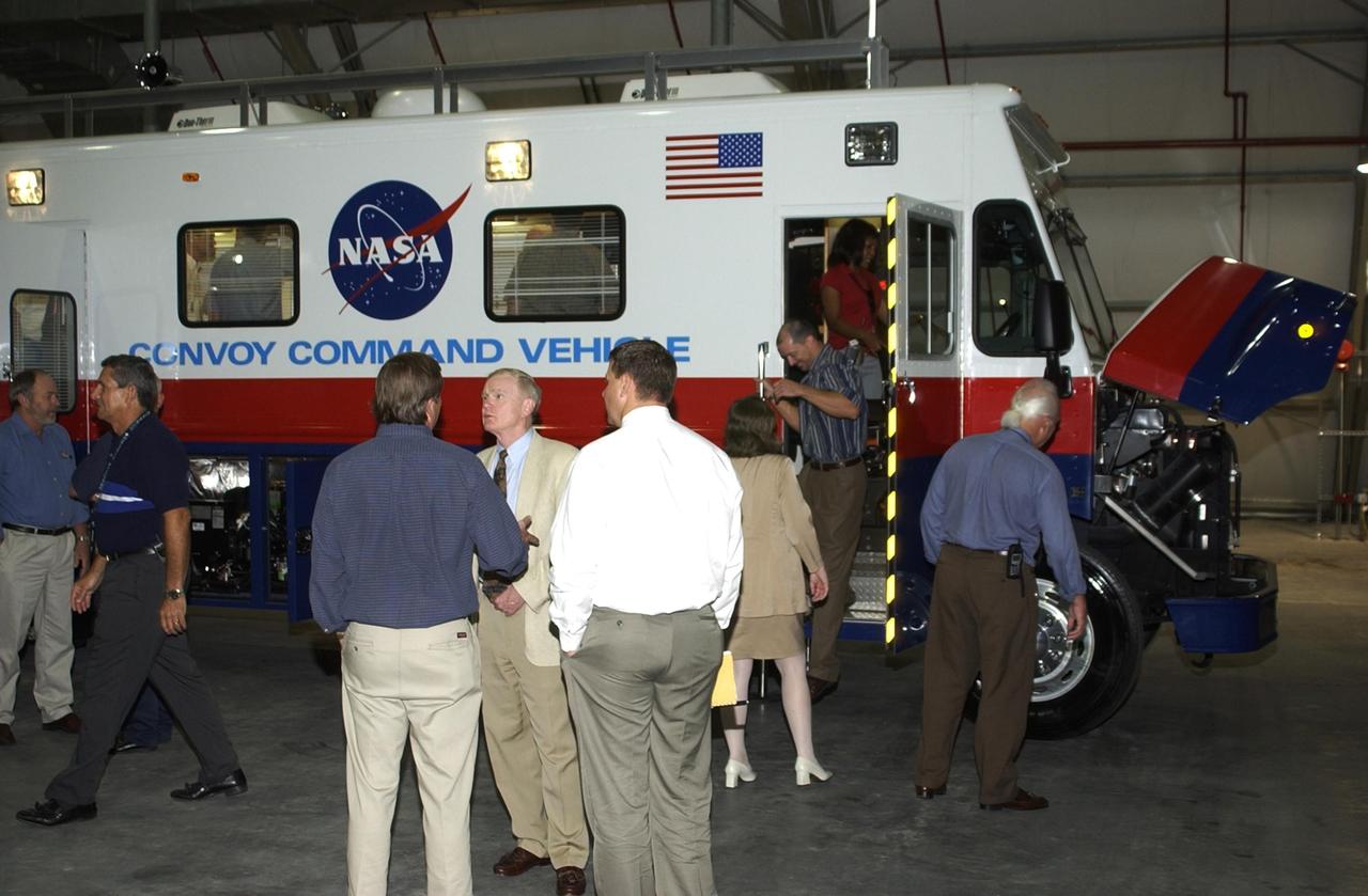 KENNEDY SPACE CENTER, FLA. --  While guests tour the new Convoy Command Vehicle (rear), Center Director Roy Bridges Jr. (center) talks to Launch Director Mike Leinbach.  The tour followed a commissioning ceremony for the new vehicle. The 40-foot vehicle is replacing a 15-year old model, and will be used following Shuttle landings as the prime vehicle to control critical communications between the orbiter, the crew and the Launch Control Center, to monitor the health of the Shuttle Orbiter systems and to direct convoy operations at the Shuttle Landing Facility. Upgrades and high-tech features incorporated into the design and development of this vehicle make it more reliable and efficient for the convoy crew. Seating capacity was increased from 4 to 12, and video recorders and television monitors were added to provide the convoy team with the maximum amount of visual information