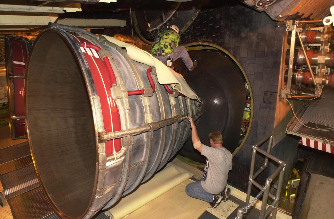 KENNEDY SPACE CENTER, FLA. -- Doug Buford (top), with the Aft Engine shop, along with another worker, removes a heat shield on one of Columbia's engines. After small cracks were discovered on the LH2 Main Propulsion System (MPS) flow liners in two other orbiters, program managers decided to move forward with inspections on Columbia before clearing it for flight on STS-107. After removal of the heat shields, the three main engines will be removed.  Inspections of the flow liners will follow.  The July 19 launch of Columbia on STS-107 has been delayed a few weeks