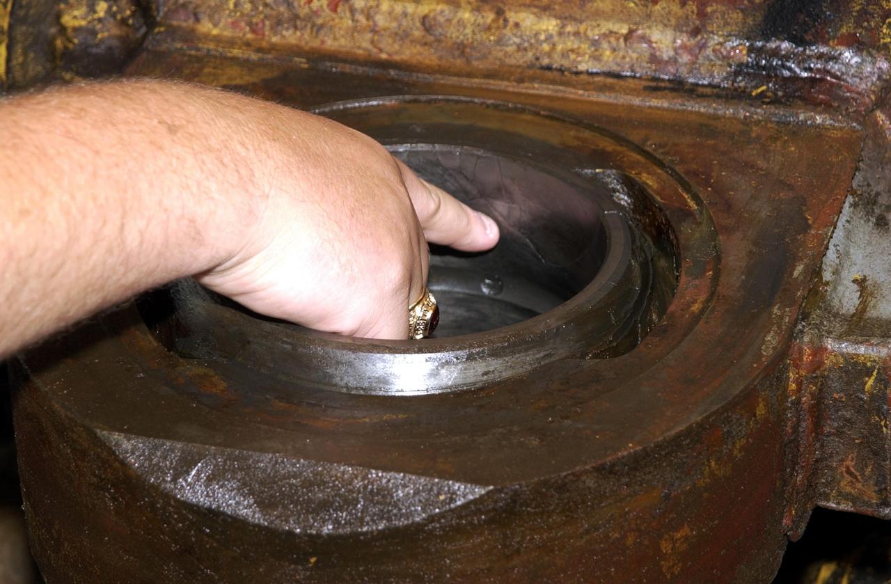 KENNEDY SPACE CENTER, FLA. -- Perry Becker, an engineer with NASA, points to a crack in a bearing from one of the jacking, equalization and leveling (JEL) cylinders on Crawler-Transporter No. 2. During inspections, technicians removed two of the 16 JEL cylinders on the vehicle to gain access to the bearings for routine maintenance and found three of the four bearings had cracks. Of the three bearings, two had extensive damage. Further eddy current inspections indicate that cracks are present on 15 of the bearings. There are 16 cylinders and 32 bearings per crawler. Although no cause for the cracks is known at this time, engineers are currently evaluating the situation to determine the most appropriate solution.