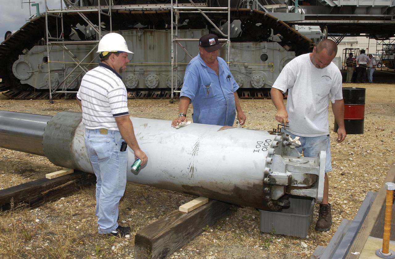 KENNEDY SPACE CENTER, FLA. -- Technicians check out a jacking, equalization and leveling (JEL) cylinders from Crawler-Transporter No. 2. During inspections, technicians removed two of the 16 JEL cylinders on the vehicle to gain access to the bearings for routine maintenance and found three of the four bearings had cracks. Of the three bearings, two had extensive damage. Further eddy current inspections indicate that cracks are present on 15 of the bearings. There are 16 cylinders and 32 bearings per crawler. Although no cause for the cracks is known at this time, engineers are currently evaluating the situation to determine the most appropriate solution.  The crawler is in the background.