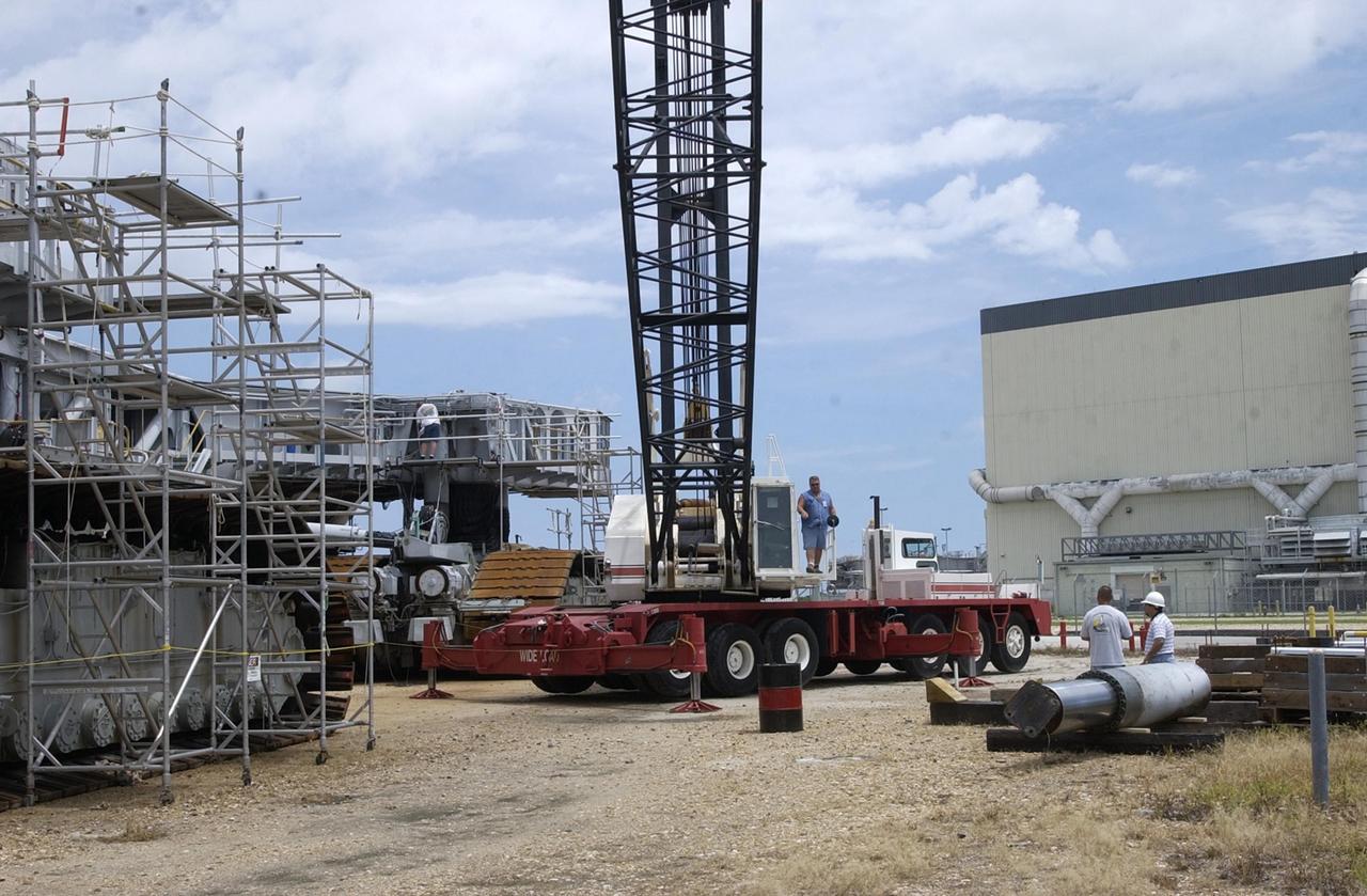 KENNEDY SPACE CENTER, FLA. --  A crane operator (center) talks with technicians (right) standing next to one of the jacking, equalization and leveling (JEL) cylinders from Crawler-Transporter No. 2. During inspections, technicians removed two of the 16 JEL cylinders on the vehicle to gain access to the bearings for routine maintenance and found three of the four bearings had cracks. Of the three bearings, two had extensive damage. Further eddy current inspections indicate that cracks are present on 15 of the bearings. There are 16 cylinders and 32 bearings per crawler. Although no cause for the cracks is known at this time, engineers are currently evaluating the situation to determine the most appropriate solution.