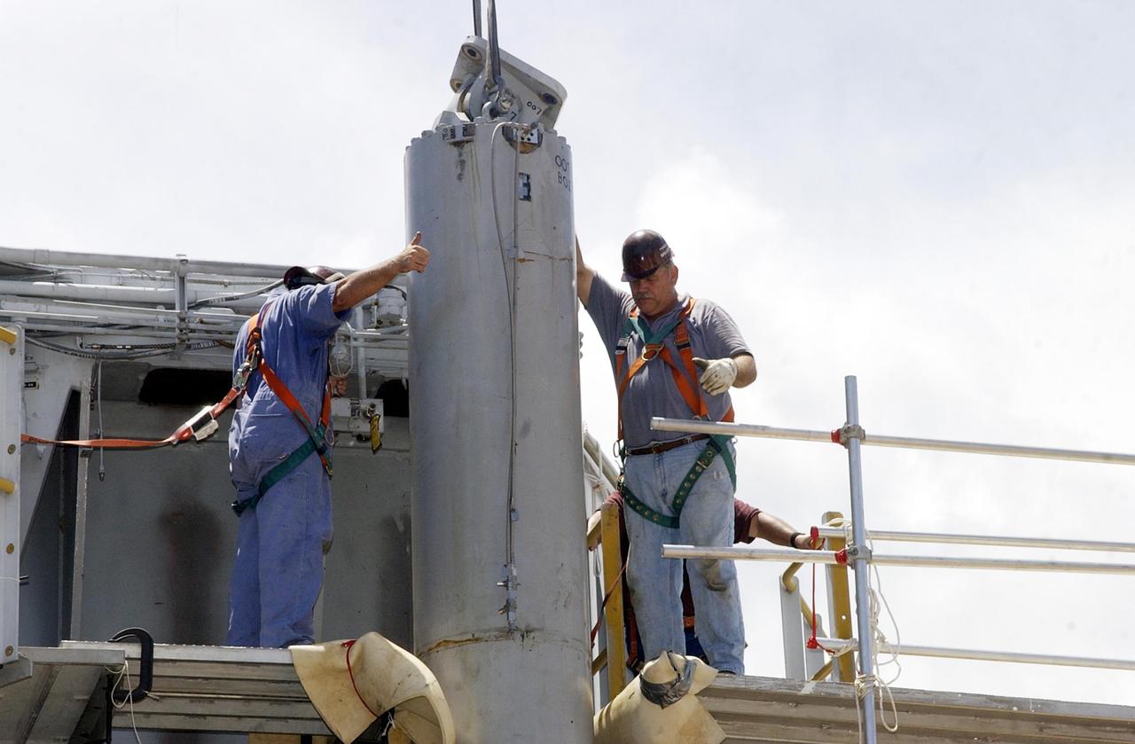 KENNEDY SPACE CENTER, FLA. -- Technicians give the signal for a crane to begin lifting a jacking, equalization and leveling (JEL) cylinder and bearing on Crawler-Transporter No. 2. During routine maintenance inspections last week, technicians removed two of the 16 JEL cylinders on the crawler to gain access to the bearings and found three of the four bearings cracked. Further eddy current inspections indicated that cracks are present on 15 of the bearings. There are 16 cylinders and 32 bearings per crawler. Engineers are evaluating the situation to determine the cause of the cracks and an appropriate solution to the problem.