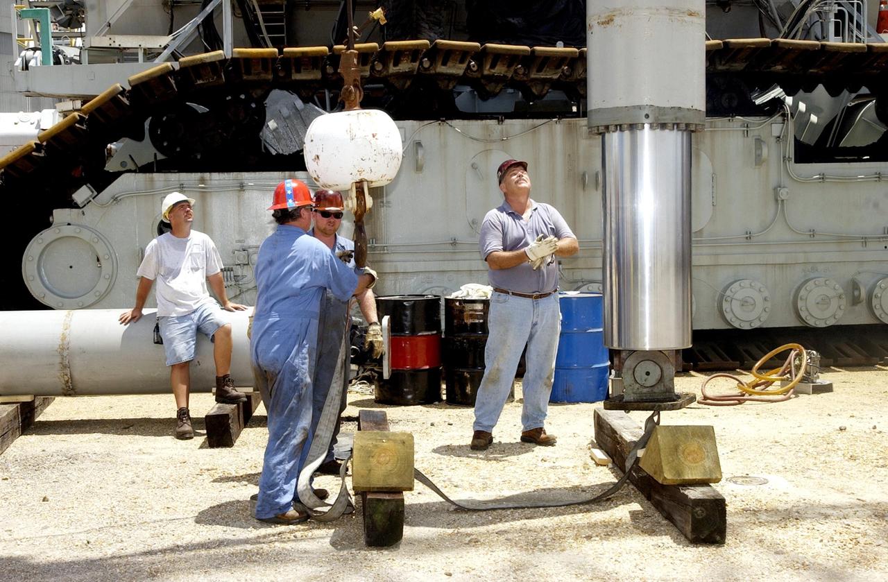 KENNEDY SPACE CENTER, FLA. -- Technicians closely monitor a jacking, equalization and leveling (JEL) cylinder and bearing from Crawler-Transporter No. 2 as it lowered  by a crane to a position on the ground. During routine maintenance inspections last week, technicians removed two of the 16 JEL cylinders on the crawler to gain access to the bearings and found three of the four bearings cracked. Further eddy current inspections indicated that cracks are present on 15 of the bearings. There are 16 cylinders and 32 bearings per crawler. Engineers are evaluating the situation to determine the cause of the cracks and an appropriate solution to the problem.