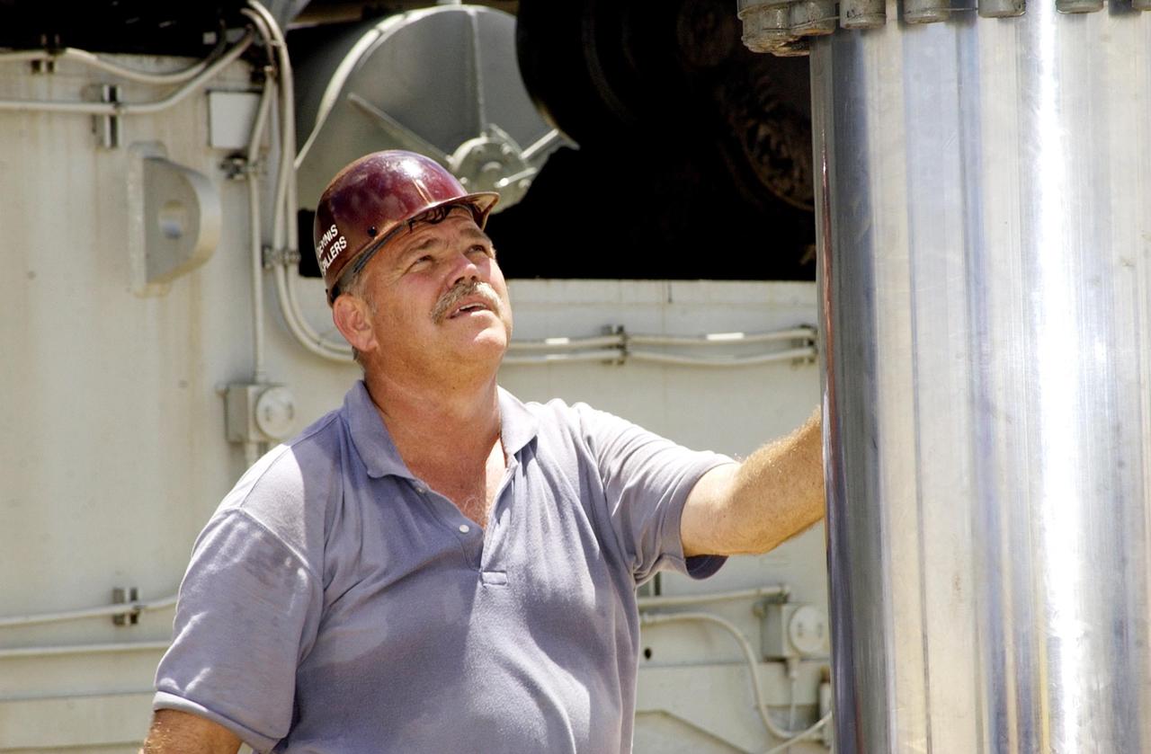 KENNEDY SPACE CENTER, FLA. -- A technician steadies a jacking, equalization and leveling (JEL) cylinder and bearing from Crawler-Transporter No. 2 as it is lowered  by a crane to a position on the ground. During routine maintenance inspections last week, technicians removed two of the 16 JEL cylinders on the crawler to gain access to the bearings and found three of the four bearings cracked. Further eddy current inspections indicated that cracks are present on 15 of the bearings. There are 16 cylinders and 32 bearings per crawler. Engineers are evaluating the situation to determine the cause of the cracks and an appropriate solution to the problem.