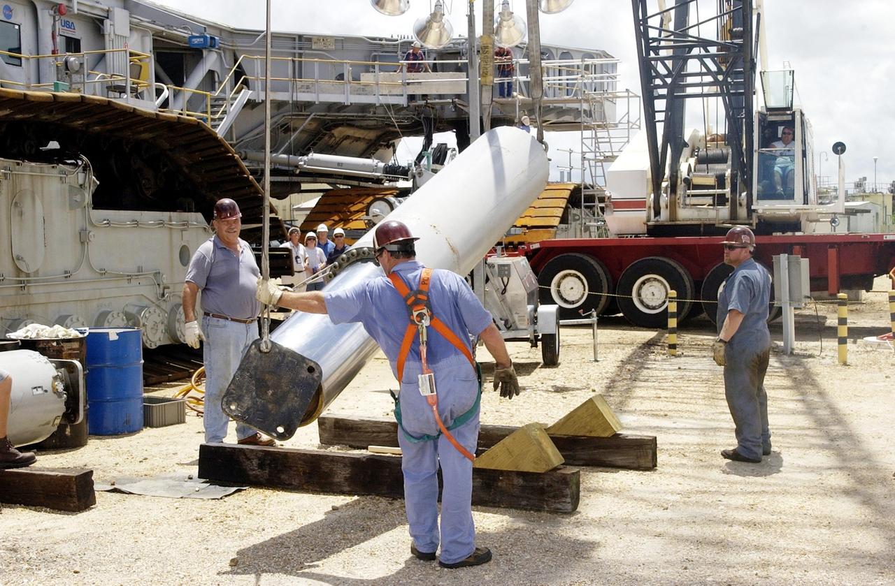 KENNEDY SPACE CENTER, FLA. -- A technician holds a crane strap to steady and guide a jacking, equalization and leveling (JEL) cylinder and bearing from Crawler-Transporter No. 2 as it is lowered  by a crane to a resting position on the ground. During routine maintenance inspections last week, technicians removed two of the 16 JEL cylinders on the crawler to gain access to the bearings and found three of the four bearings cracked. Further eddy current inspections indicated that cracks are present on 15 of the bearings. There are 16 cylinders and 32 bearings per crawler. Engineers are evaluating the situation to determine the cause of the cracks and an appropriate solution to the problem.