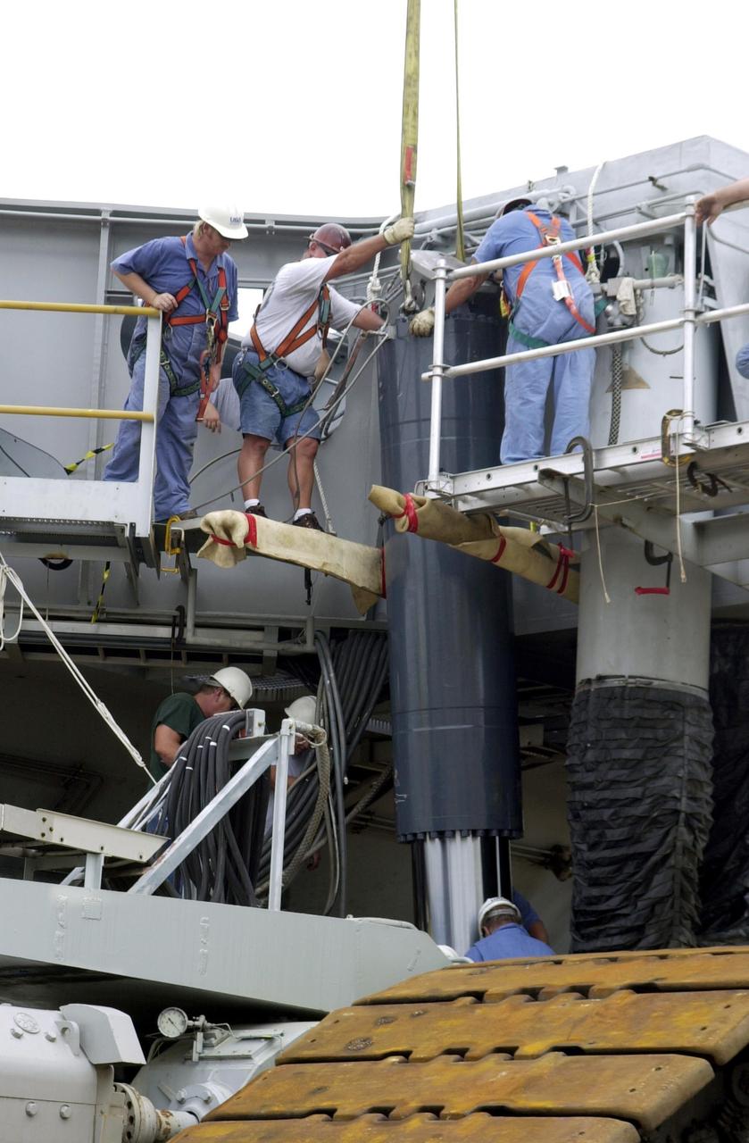 KENNEDY SPACE CENTER, FLA. -- Workers on Crawler Transporter No. 2 help guide a repaired Jacking, Equalization and Leveling (JEL) cylinder as it is lowered into place. There are 16 cylinders and 32 bearings per crawler.  During recent routine maintenance inspections, technicians removed two of the 16 JEL cylinders on the crawler to gain access to the bearings and found three of the four bearings cracked.  Further eddy current inspections indicated that cracks were present on 15 of the bearings.. Technicians have removed and replaced 14 of the bearings on  CT-2, which is being repaired in order to enable Atlantis' rollout for mission STS-112, scheduled for launch no earlier than Oct. 2.