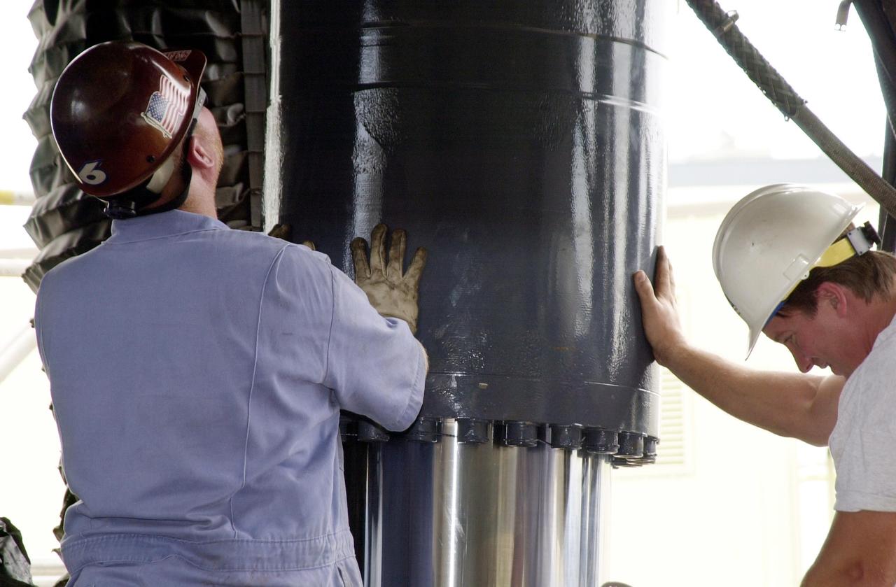 KENNEDY SPACE CENTER, FLA. --  Two workers help maneuver a repaired Jacking, Equalization and Leveling (JEL) cylinder as it is lowered into place on Crawler Transporter No. 2. There are 16 cylinders and 32 bearings per crawler.  During recent routine maintenance inspections, technicians removed two of the 16 JEL cylinders on the crawler to gain access to the bearings and found three of the four bearings cracked.  Further eddy current inspections indicated that cracks were present on 15 of the bearings.. Technicians have removed and replaced 14 of the bearings on  CT-2, which is being repaired in order to enable Atlantis' rollout for mission STS-112, scheduled for launch no earlier than Oct. 2.