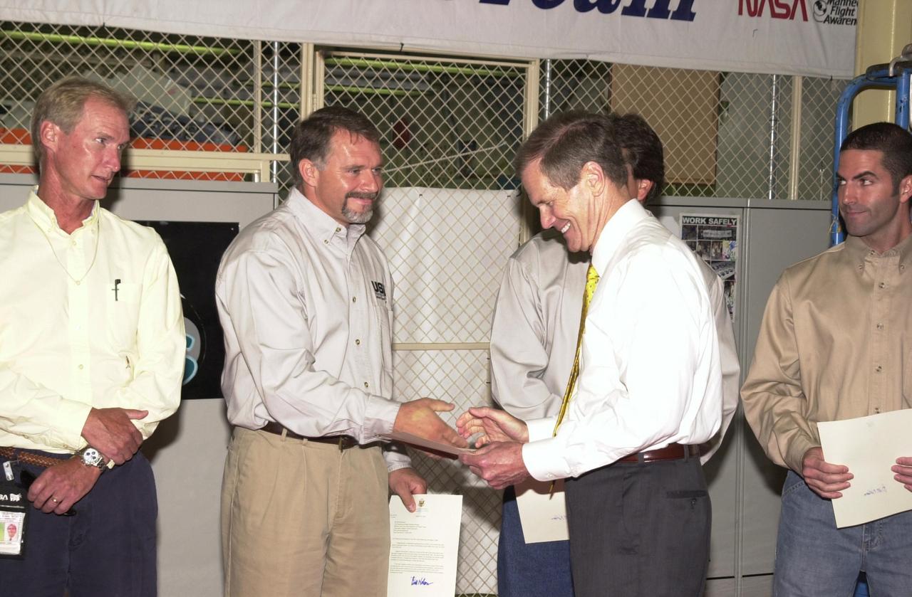 KENNEDY SPACE CENTER, FLA. --  U.S. Sen. Bill Nelson congratulates Jerry Goudy with the Flow Liner Inspection & Repair team.  Nelson presented gold seal Senate certificates to the team for their work on finding the cracks in orbiter flow liners and repairing them.  At left is Mike Young, behind Nelson is Tony Nesotas, at right is David Strait, who found the first fuel-line crack. Not pictured is Rick Beckwith.   