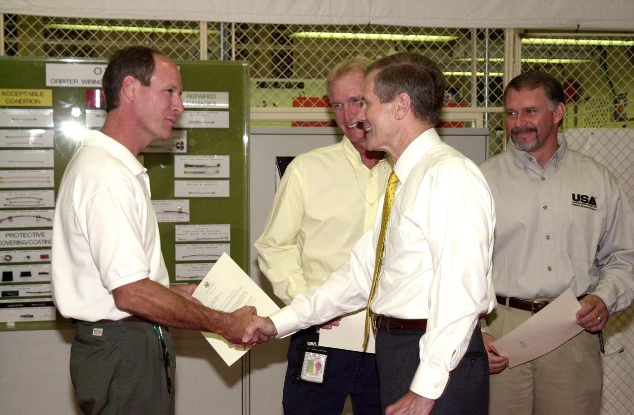 KENNEDY SPACE CENTER, FLA. -- U.S. Sen. Bill Nelson congratulates Rick Beckwith, with the Flow Liner Inspection & Repair team.  Nelson presented gold seal Senate certificates to the team for their work on finding the cracks in orbiter flow liners  and repairing them.  Other team members behind Nelson are Mike Young (center) and Jerry Gouding (right).  Not pictured are Tony Nesotas and David Strait. Strait first spotted the fuel-line crack; Goudy performed arc welding on one of Atlantis' flow liners.    