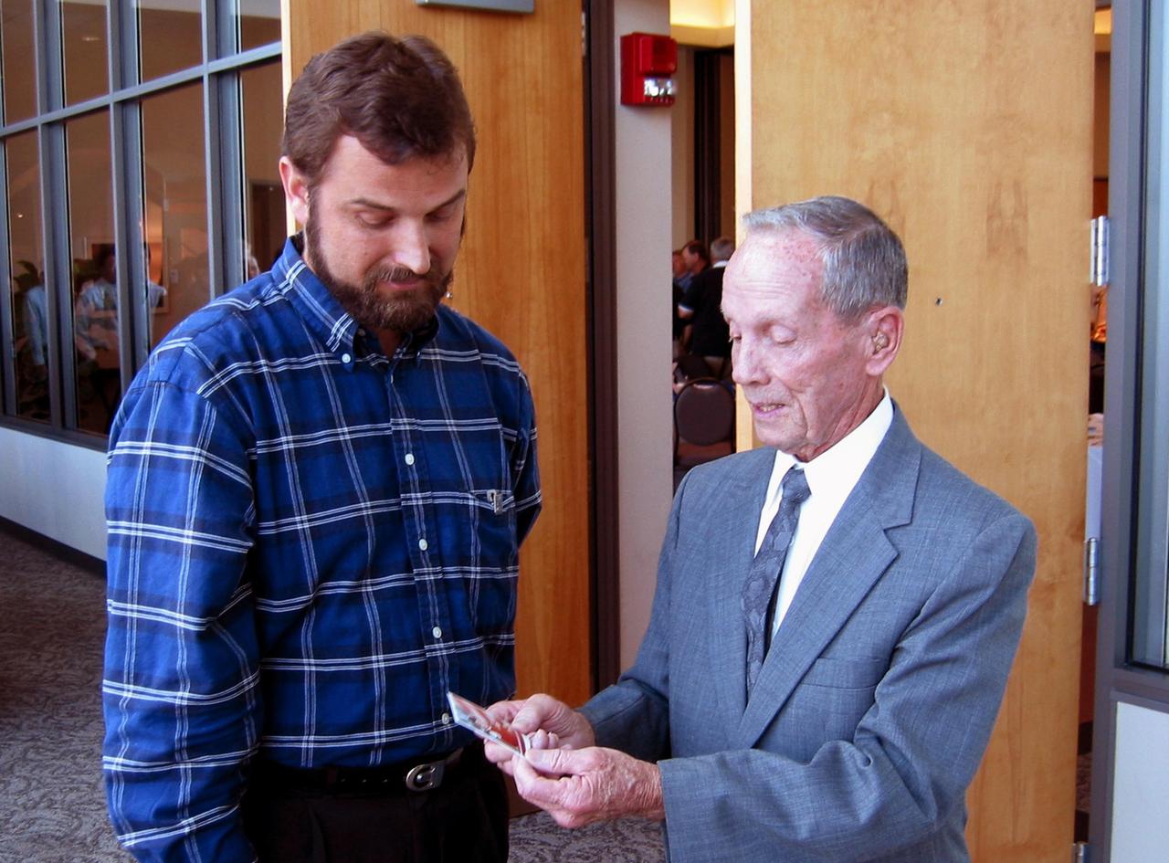 KENNEDY SPACE CENTER, FLA. - Adam Kissiah (right), a retired NASA-KSC engineer, looks at a photo of Allan Dianic's daughter, who has benefited from a cochlear implant that Kissiah developed while at NASA.  Dianic (left) is a software engineer with ENSCO.  Kissiah received an exceptional category NASA Space Act Award for his 25-year-old technology breakthrough during a technology awards luncheon held at the KSC Visitor Complex Debus Center.   The award included a monetary award and a certificate signed by the NASA Administrator.  Space Act Awards provide official recognition and grant equitable monetary awards for inventions and scientific and technical contributions that have helped achieve NASA's aeronautical and space goals.
