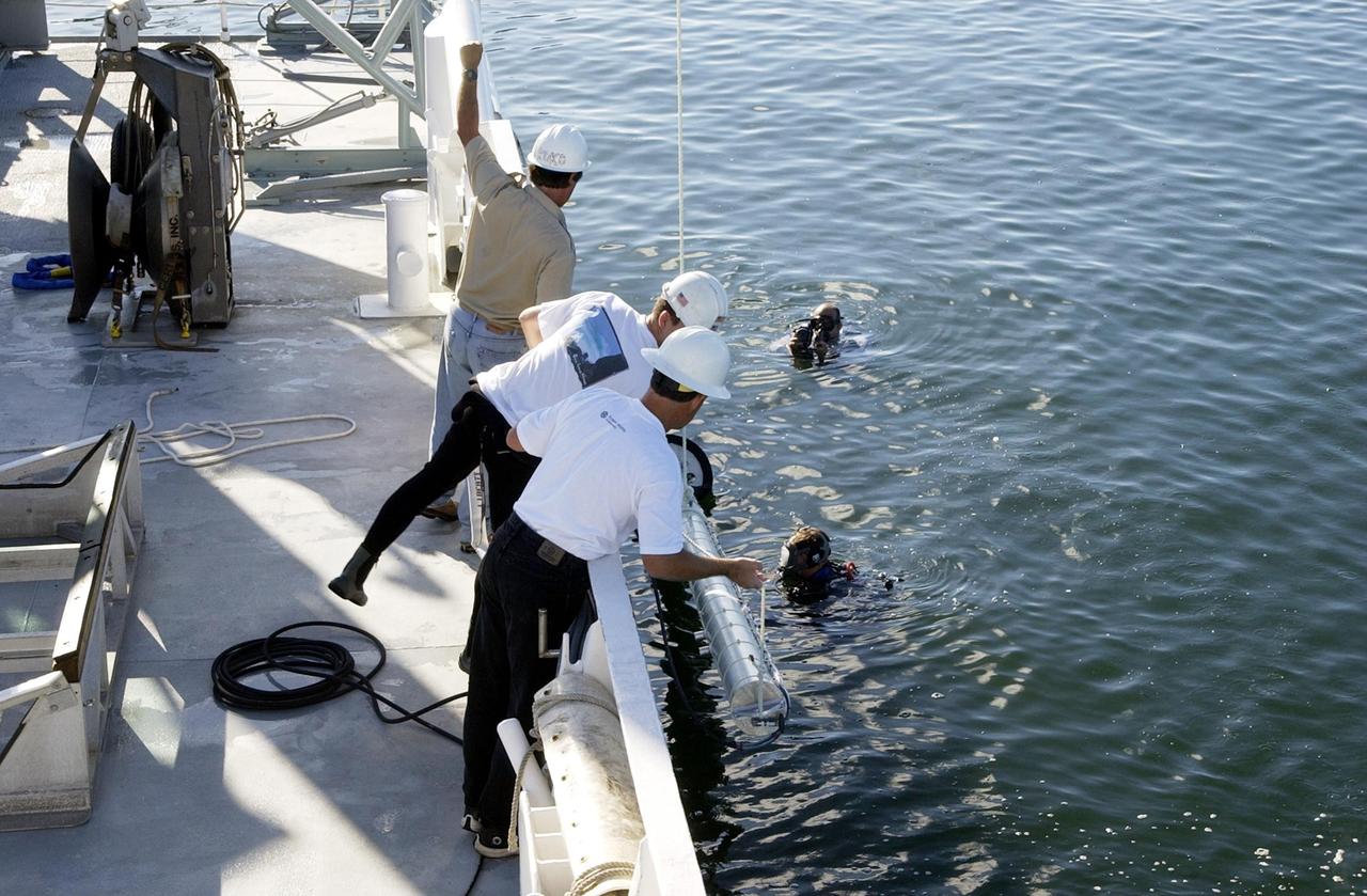 KENNEDY SPACE CENTER, FLA. -- Workers on the deck of the Liberty Star, one of NASA's solid rocket booster retrieval ships, as well as divers in the water, help lower sonar mapping equipment alongside the ship. The equipment will be attached to the ship's hull for an eight-day expedition surveying deep-water coral reefs on the Oculina Banks off eastern Florida. NASA joins the National Oceanic and Atmospheric Administration (NOAA) and other ocean scientists for the sophisticated mapping system that will provide the first high-resolution, three-dimensional map of the Oculina Banks. The survey results are expected to guide another expedition in Spring 2003, using NASA's ship, when the reef fish spawn. Also used will be NASA's underwater robot and an acoustic hydrophone system for listening to fish and vessel noise. Dive sites will be chosen based on the new charts.